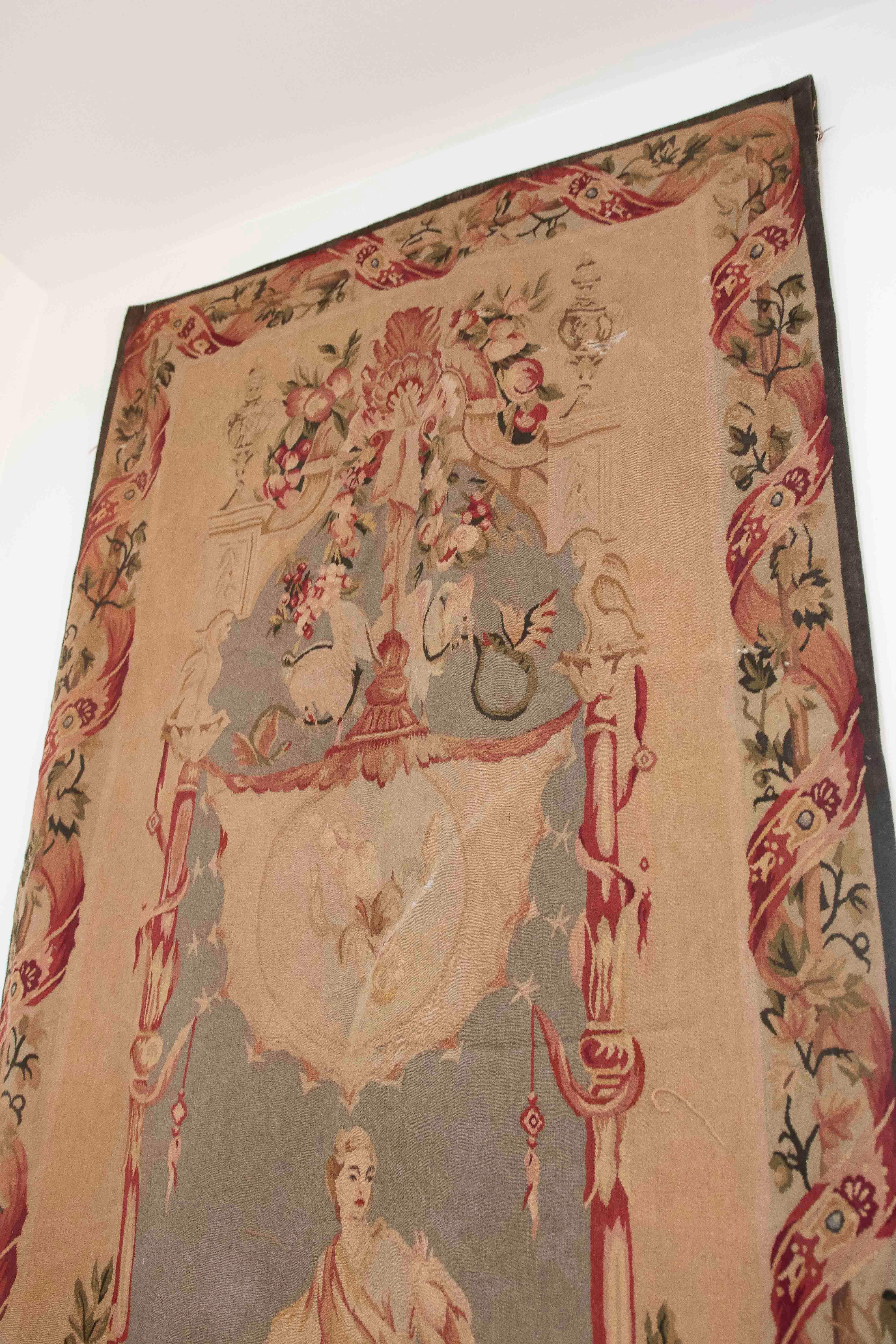 Questo grande arazzo verticale presenta una scena allegorica riccamente ornata, probabilmente tessuta nella tradizione dei laboratori europei del XVIII secolo, forse francesi o fiamminghi. Al centro della composizione c'è un'elegante figura