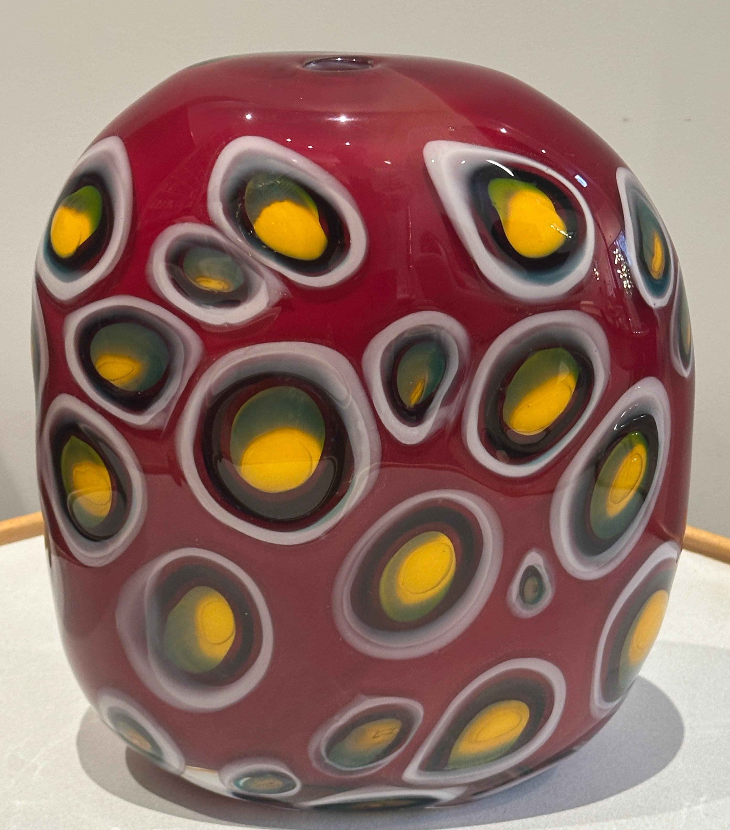 1990s American contemporary decorative handblown art glass vase.  The vase features a distinctive deep red body.  The surface is adorned with multiple floating, amoeba-like shapes of varying sizes, outlined in white with a yellow-green and black