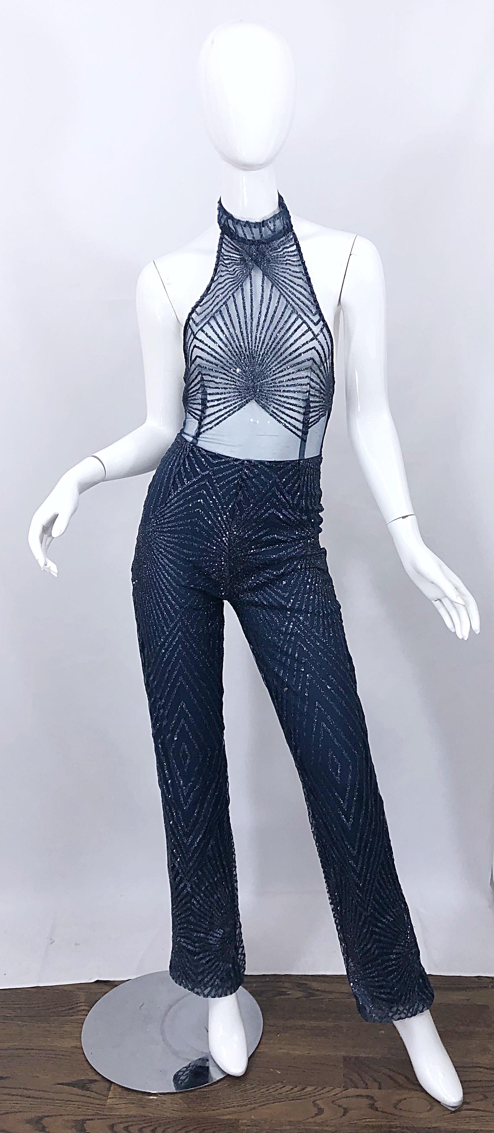 Sexy 1990s does 1970s navy blue semi sheer mesh glitter halter jumpsuit! Features a flattering high neck. Glitter patterned in zigzags throughout. High neck with two ivory pearl buttons at top back neck, and hidden zipper up the pants (which are