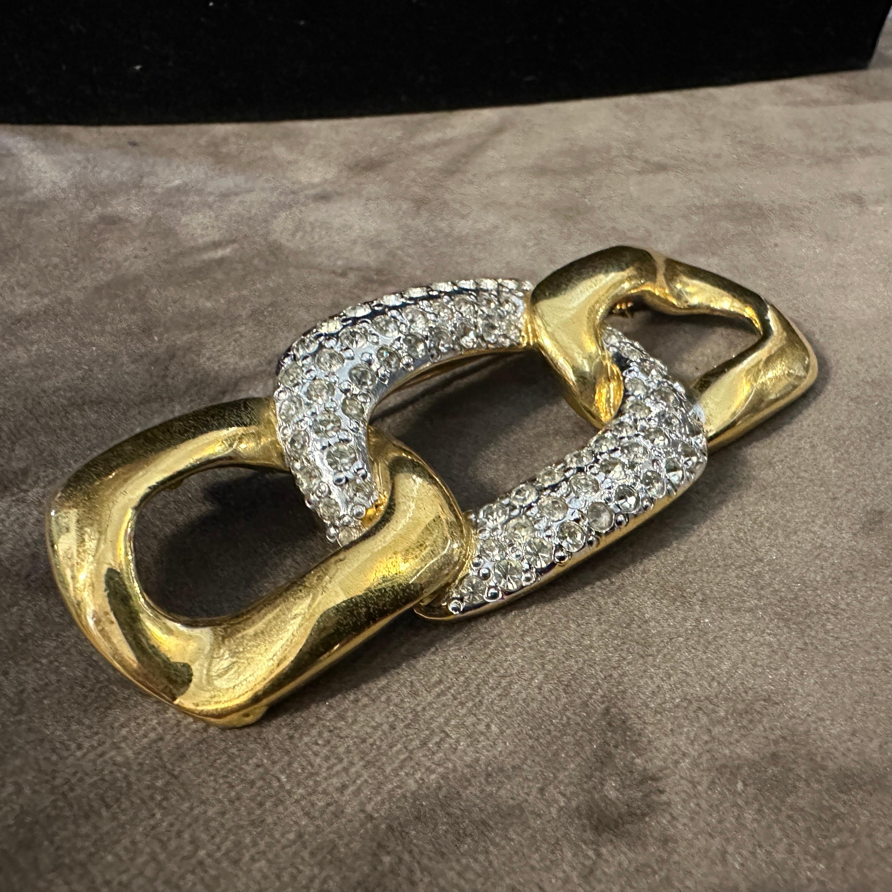 This 1990s Yves Saint Laurent (YSL) costume jewelry brooch is an exquisite example of the bold, glamorous aesthetic for which the brand was renowned. The brooch consists of three interlocking, sculptural links that form a dynamic and elegant