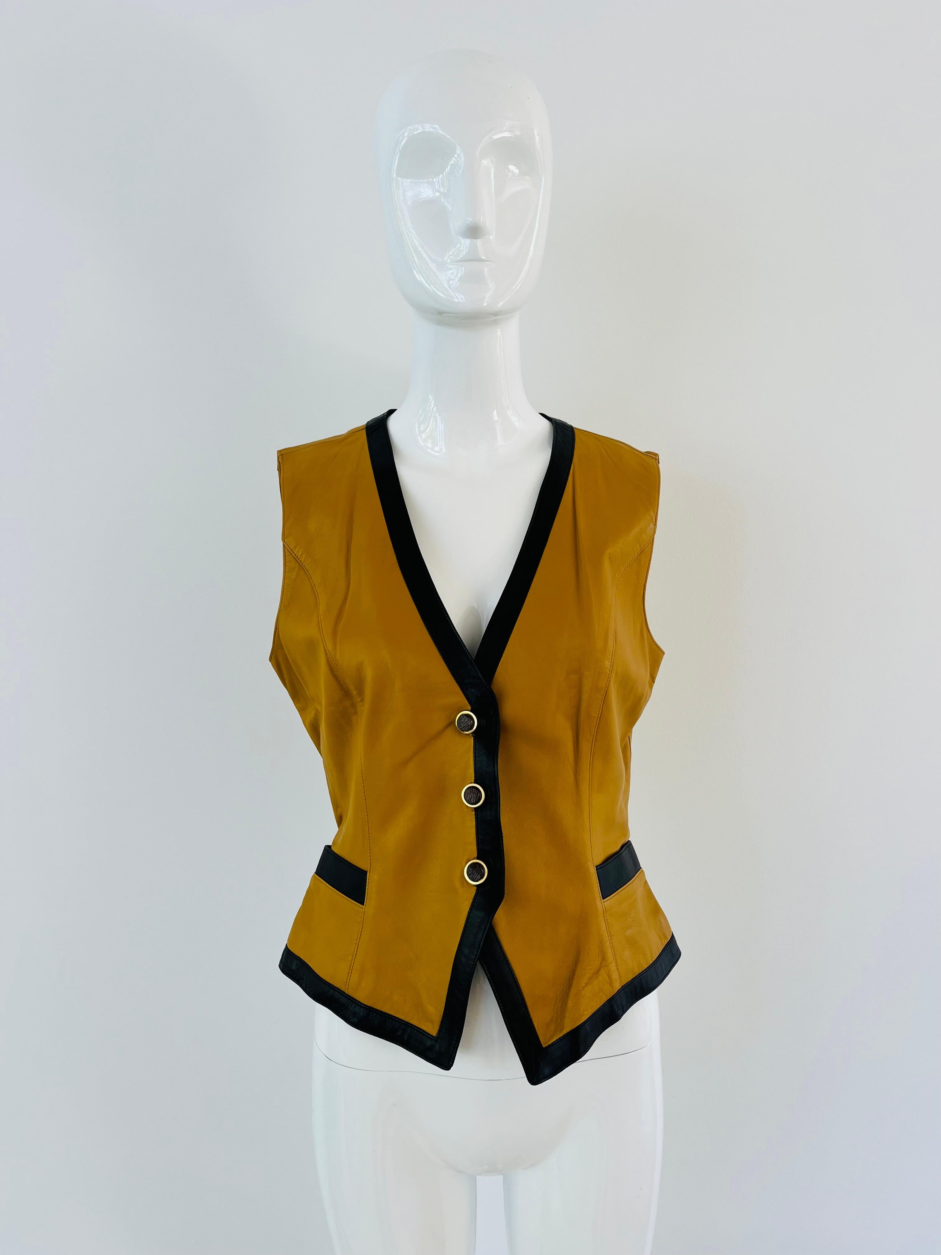 1990s Vintage Emanuel Ungaro mustard yellow/brown and black trim soft leather vest, with wood and gold hardware buttons. Two front pockets with contrasting trim. Fabric label is missing but leather and lined in acetate. Marked as a size 8 and