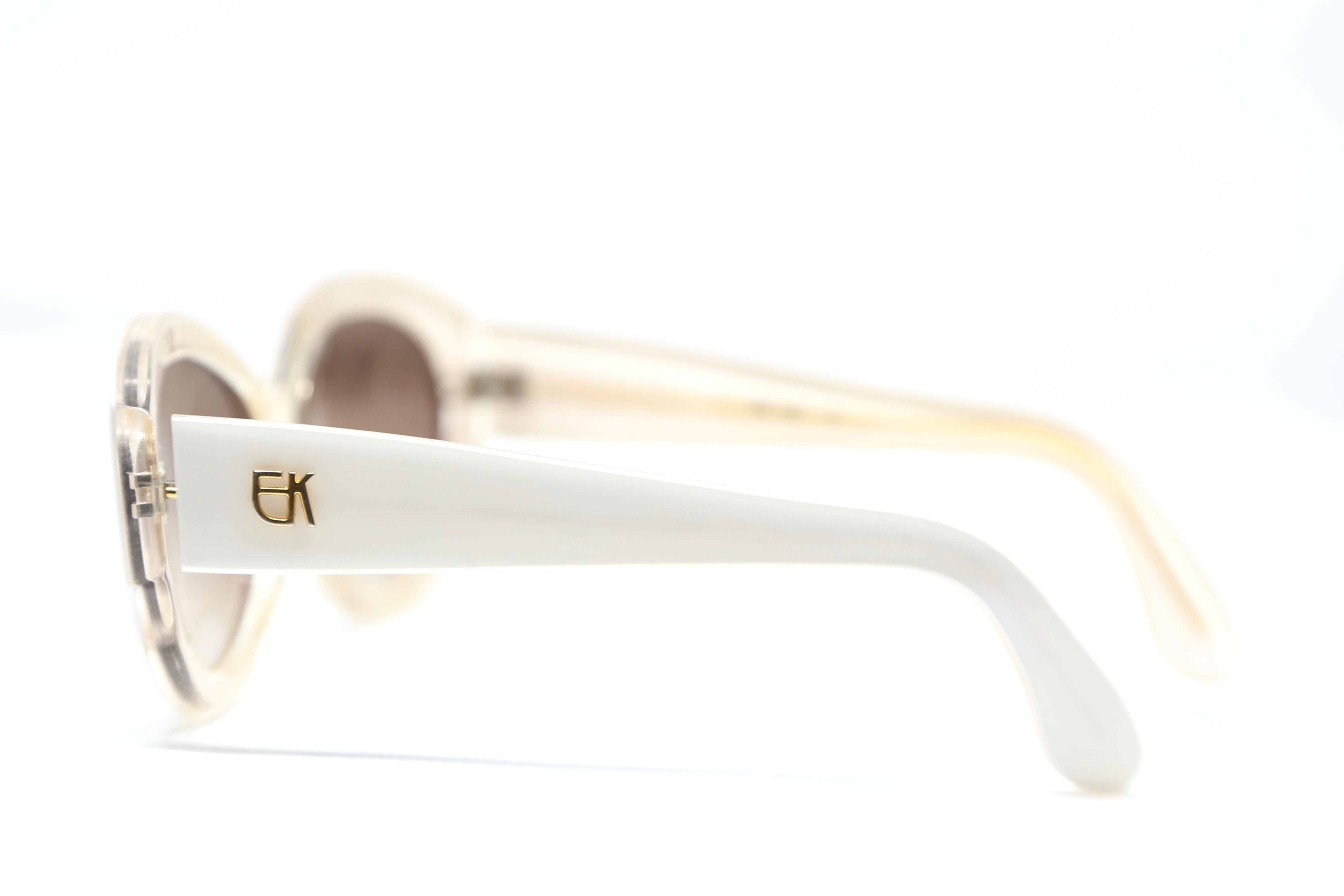 Opaque white plastic sunglasses fused with clear backing and gold-toned metal EK logos at temples designed by Emmanuelle Khanh dating to the late 1980's, early 1990's. Frames work well for a narrow head (fit snugly). Approximate measurements: 5.5