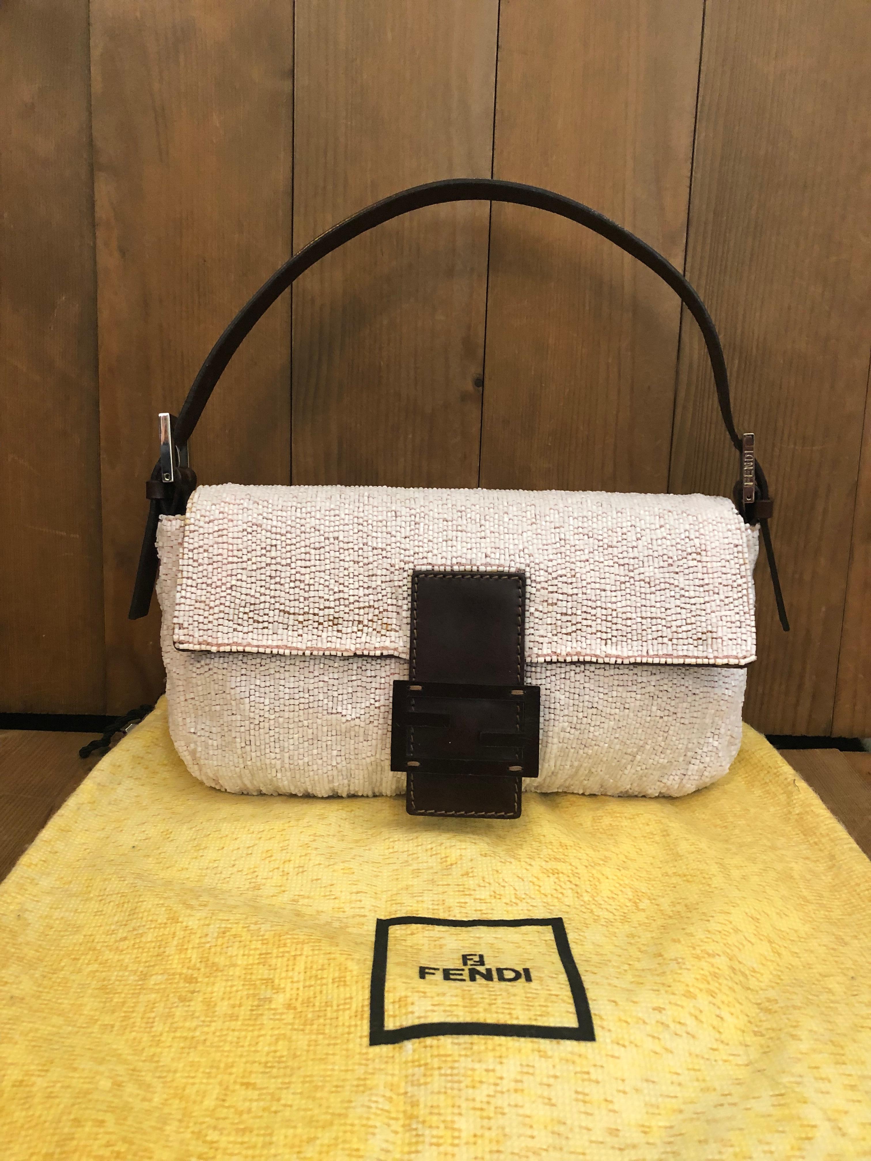 This iconic Fendi Baguette hand bag is crafted of and covered in pale pink beads with dark brown leather and satin interior featuring one interior zip pocket. Made in Italy. Magnetic snap fastening. Measures 10 x 5.5 x 2 inches Drop 6. Comes with