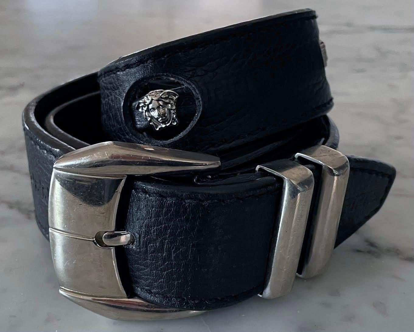 Texturierter schwarzer Ledergürtel mit griechischer Schlüsselprägung und Ausschnitten mit silberfarbenen Medusa-Köpfen, entworfen von Gianni Versace in den 1990er Jahren. Der Gürtel ist mit der Größe 70 gekennzeichnet. Die Gürtellöcher liegen bei