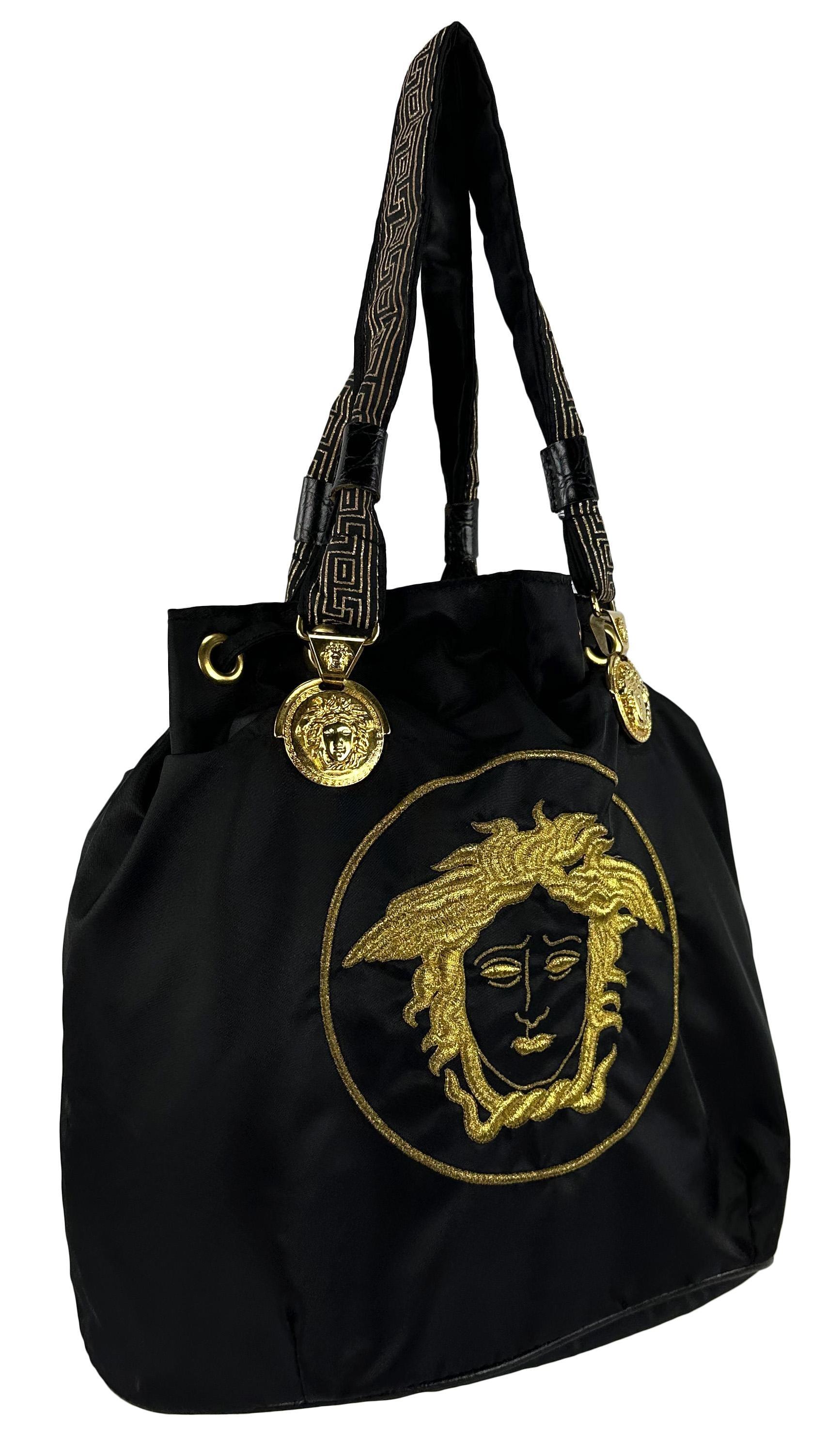 Datant des années 1990, ce fourre-tout en nylon noir de Gianni Versace arbore une grande Méduse de Versace brodée sur le devant. Il est rehaussé de reliefs de la Méduse de Versace en ton or à la base de chaque sangle, ce qui en fait le sac Versace