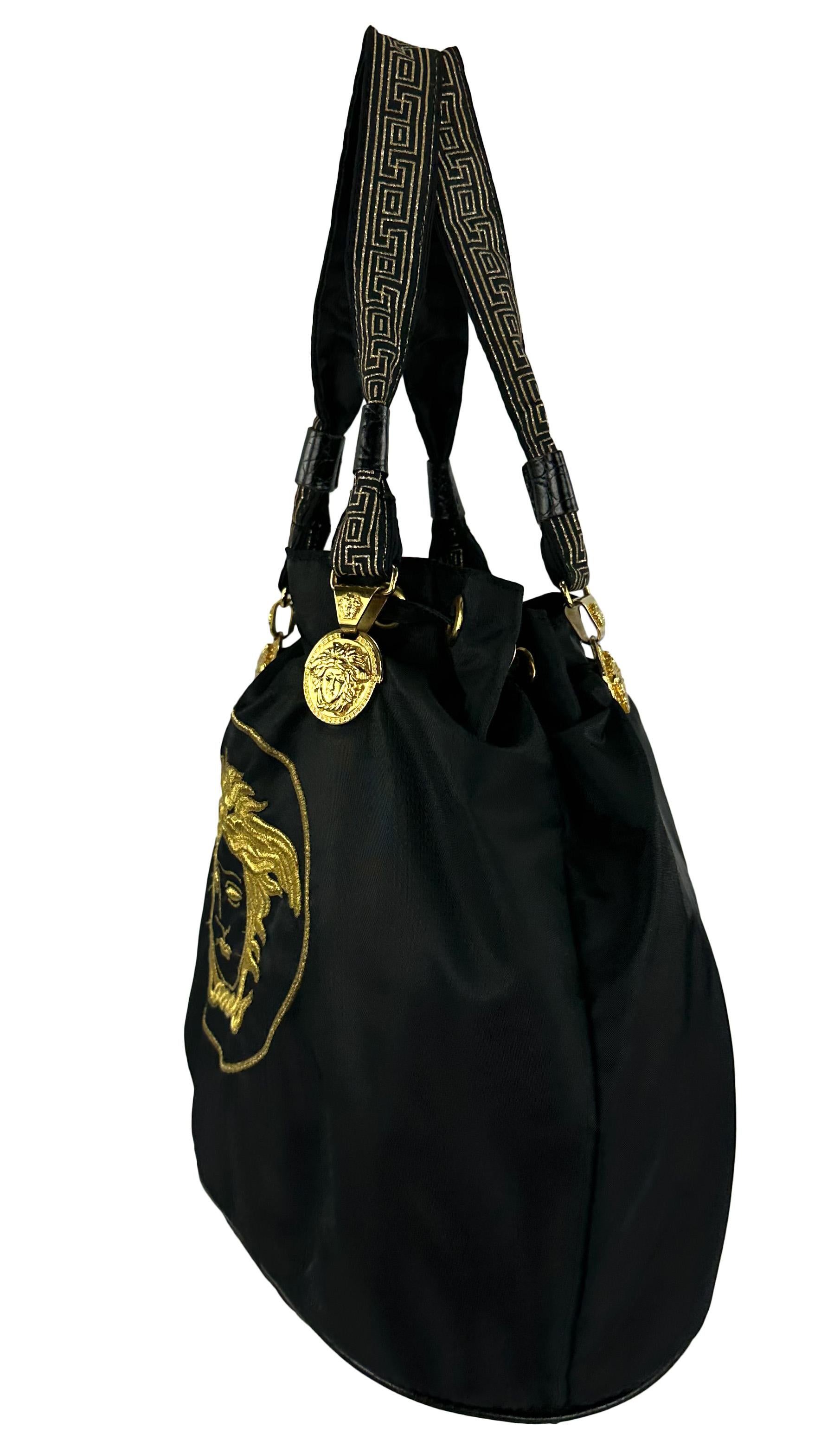 Datant des années 1990, ce fourre-tout en nylon noir de Gianni Versace arbore une grande Méduse de Versace brodée sur le devant. Il est rehaussé de reliefs de la Méduse de Versace en ton or à la base de chaque sangle, ce qui en fait le sac Versace