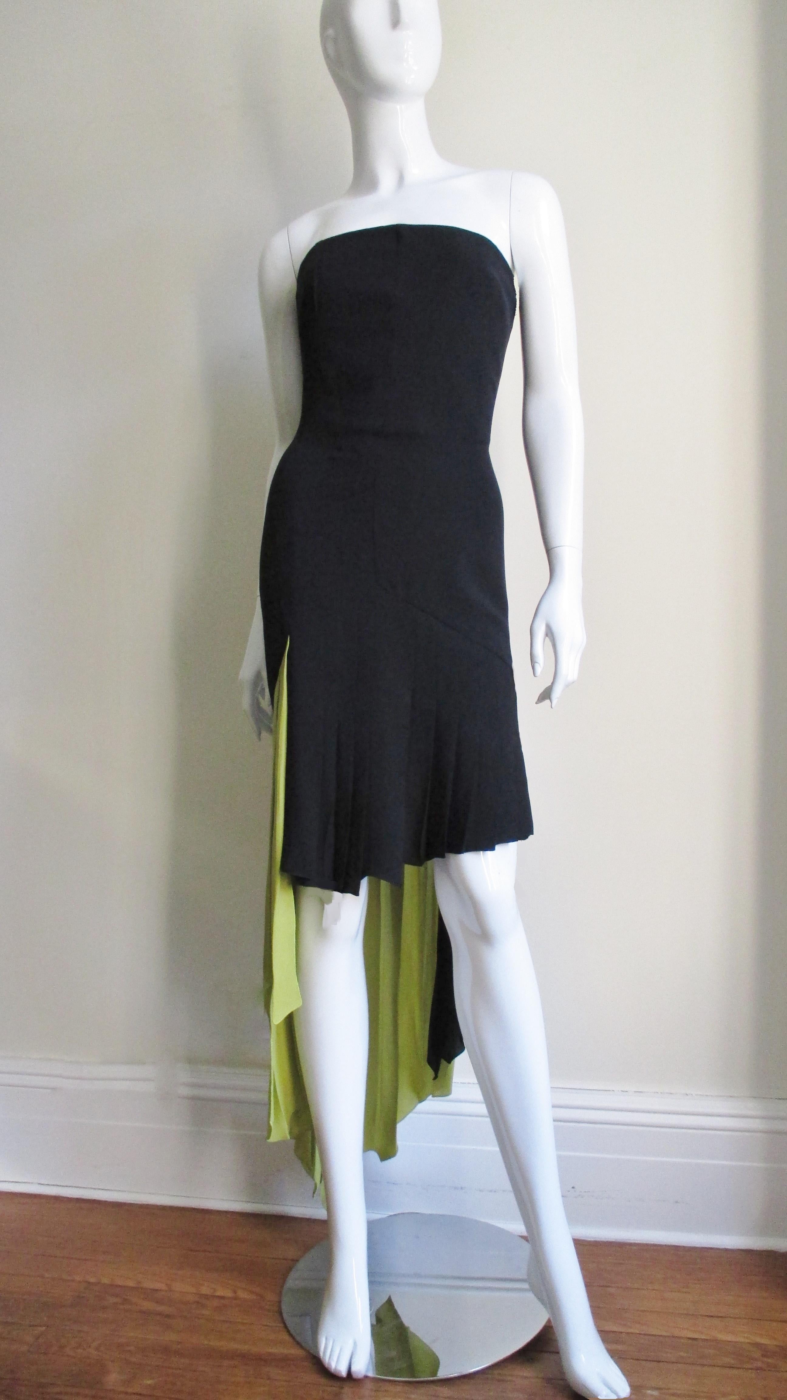 A silk bustier color block dress in black and lime green with a high low asymmetrical pleated hemline from Gianni Versace. The strapless dress has an inner boned corset for support. It is semi fitted through to the hips then falls in varying lengths