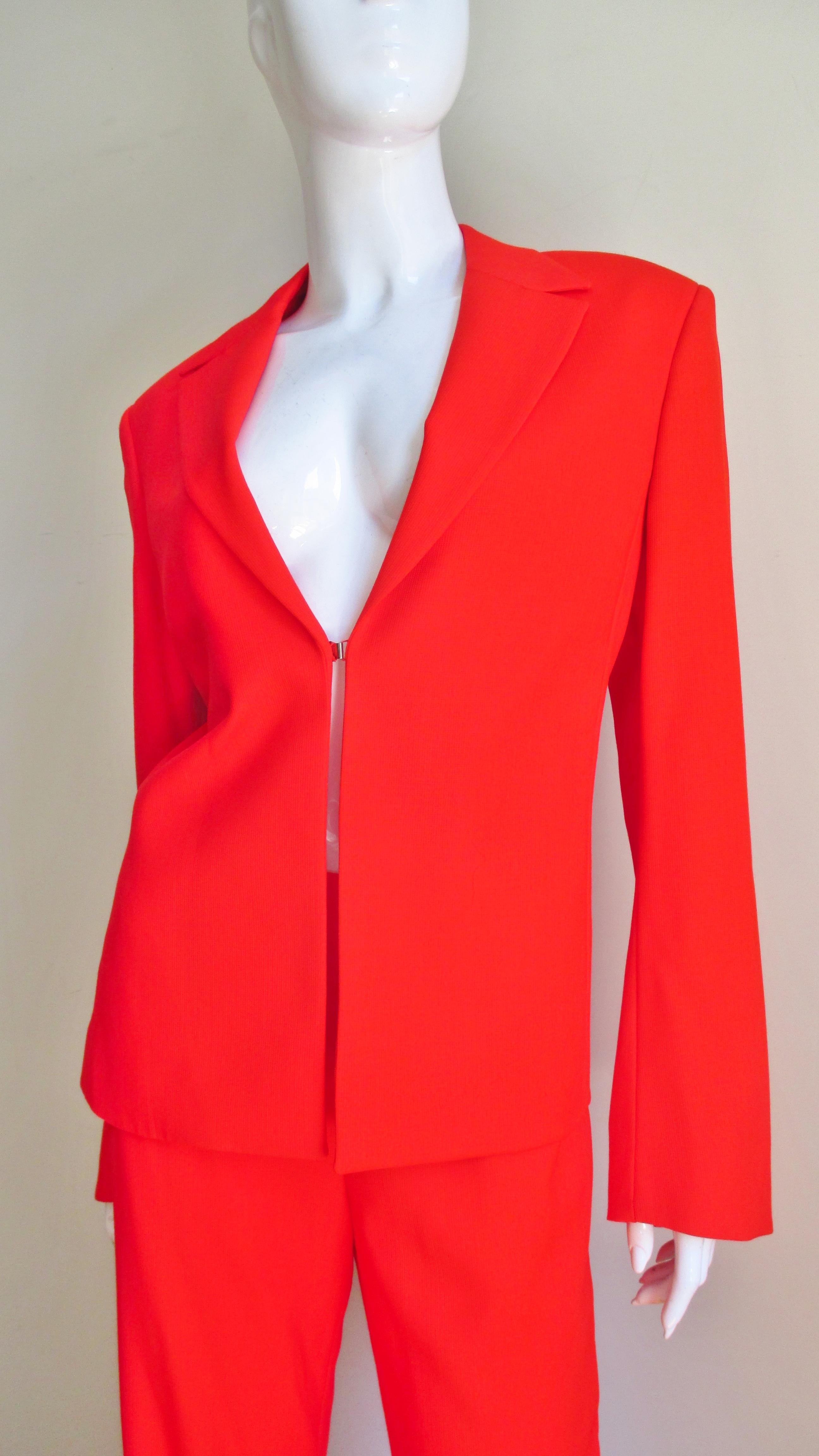 A gorgeous orange light weight wool pant suit from Gianni Versace Couture.  The lapel jacket has a front hook closure and lightly padded shoulders.  The straight leg mid rise pants have 2 narrow curved nude mesh covered cut outs at each side upper