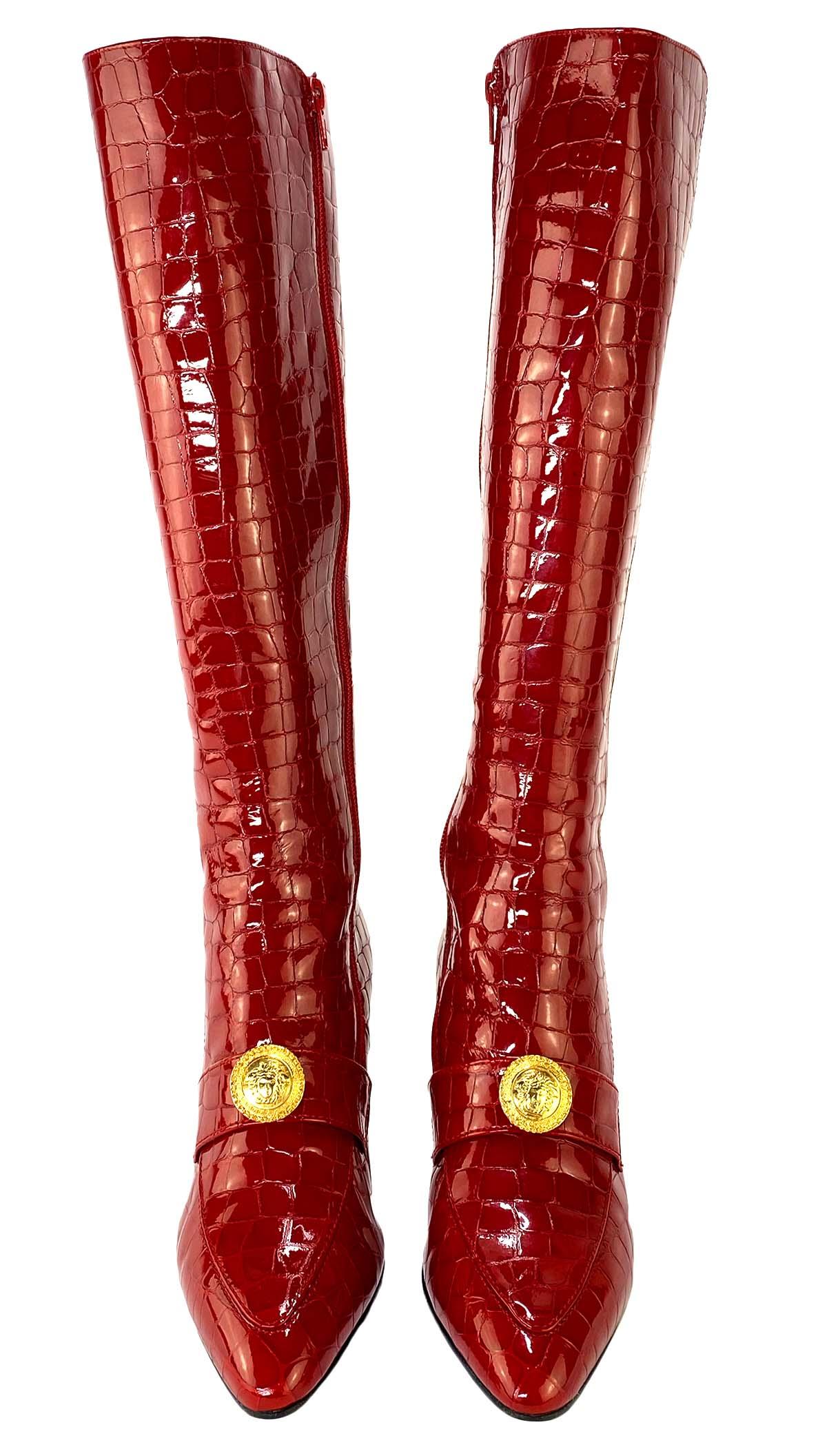 TheRealList presents: a pair of red hot crocodile embossed Gianni Versace boots, designed by Gianni Versace. These stunning heels boots are from the 1990s and feature a golden Medusa emblem on the top of the shoe. The patent leather is embossed with