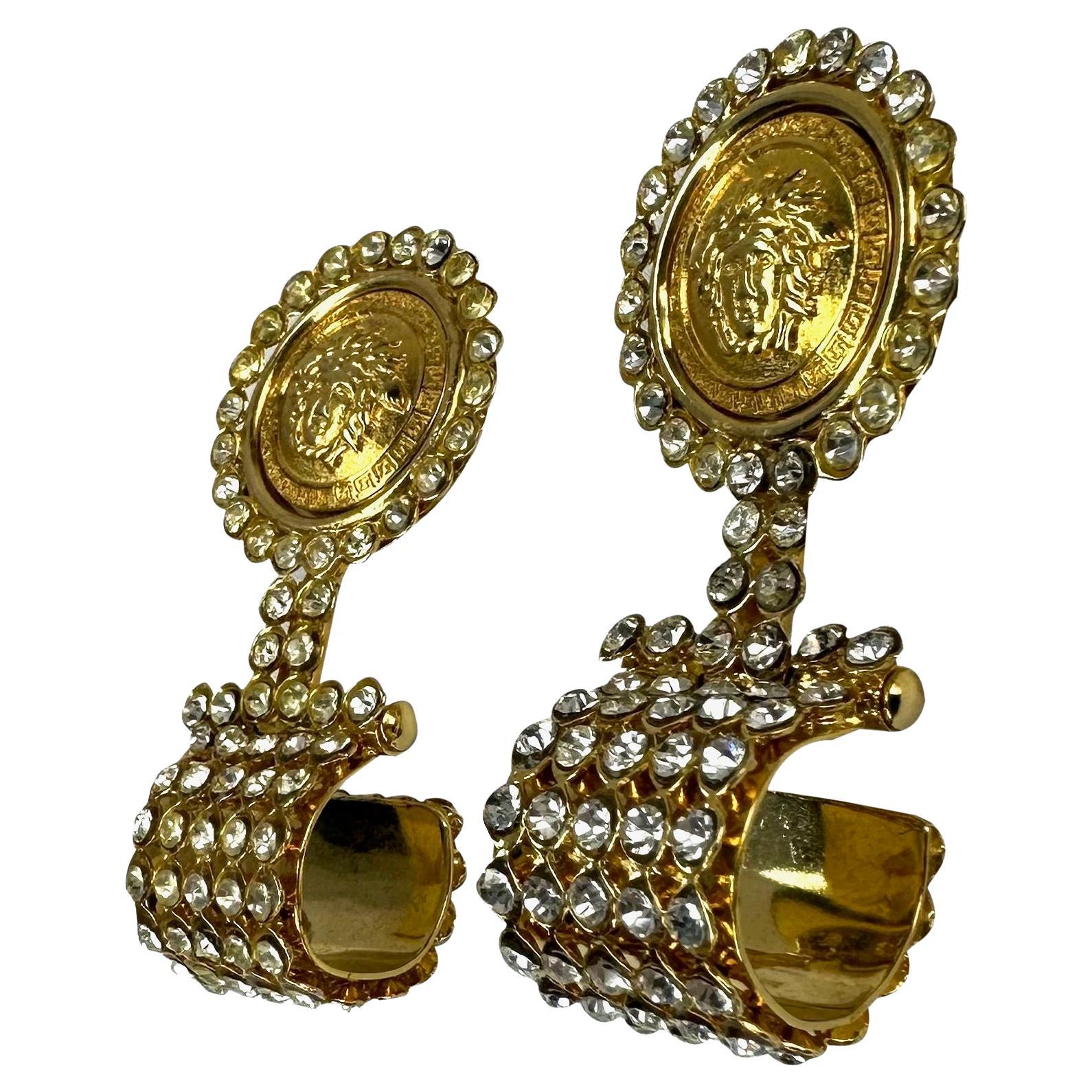 Presenting a pair of beautiful gold-tone Gianni Versace clip-on earrings, designed by Gianni Versace. From the 1990s, these fabulous costume earrings feature a Versace Medusa relief surrounded by rhinestones and a rhinestone drop. The perfect glitzy
