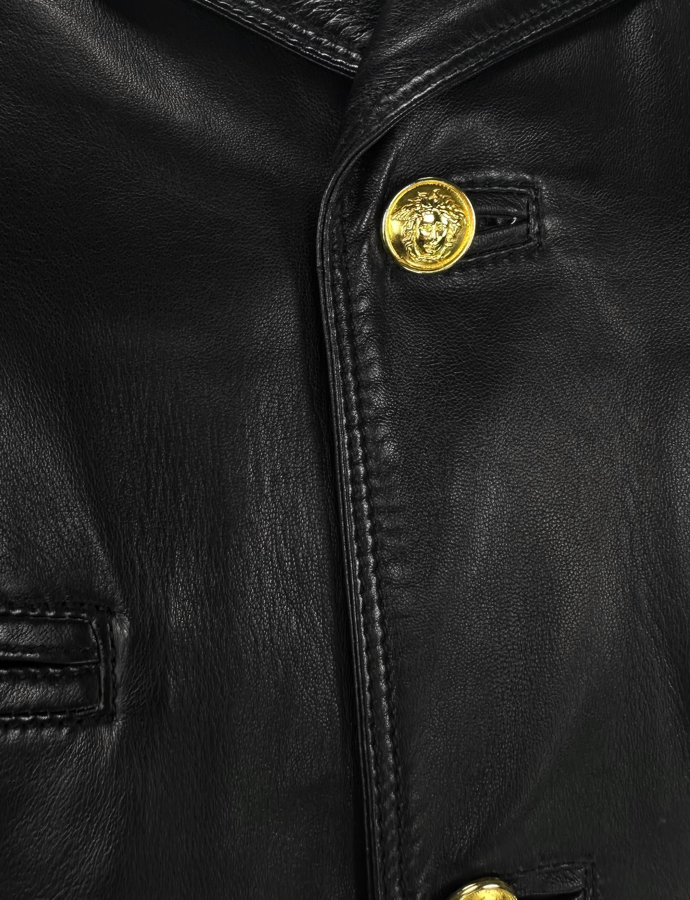 Questo cappotto oversize da uomo in pelle nera, disegnato da Gianni Versace negli anni '90, presenta un colletto ripiegato, bottoni a rilievo Medusa in oro e tasche sul petto e sui fianchi. Realizzato interamente in pelle, è un pezzo forte che