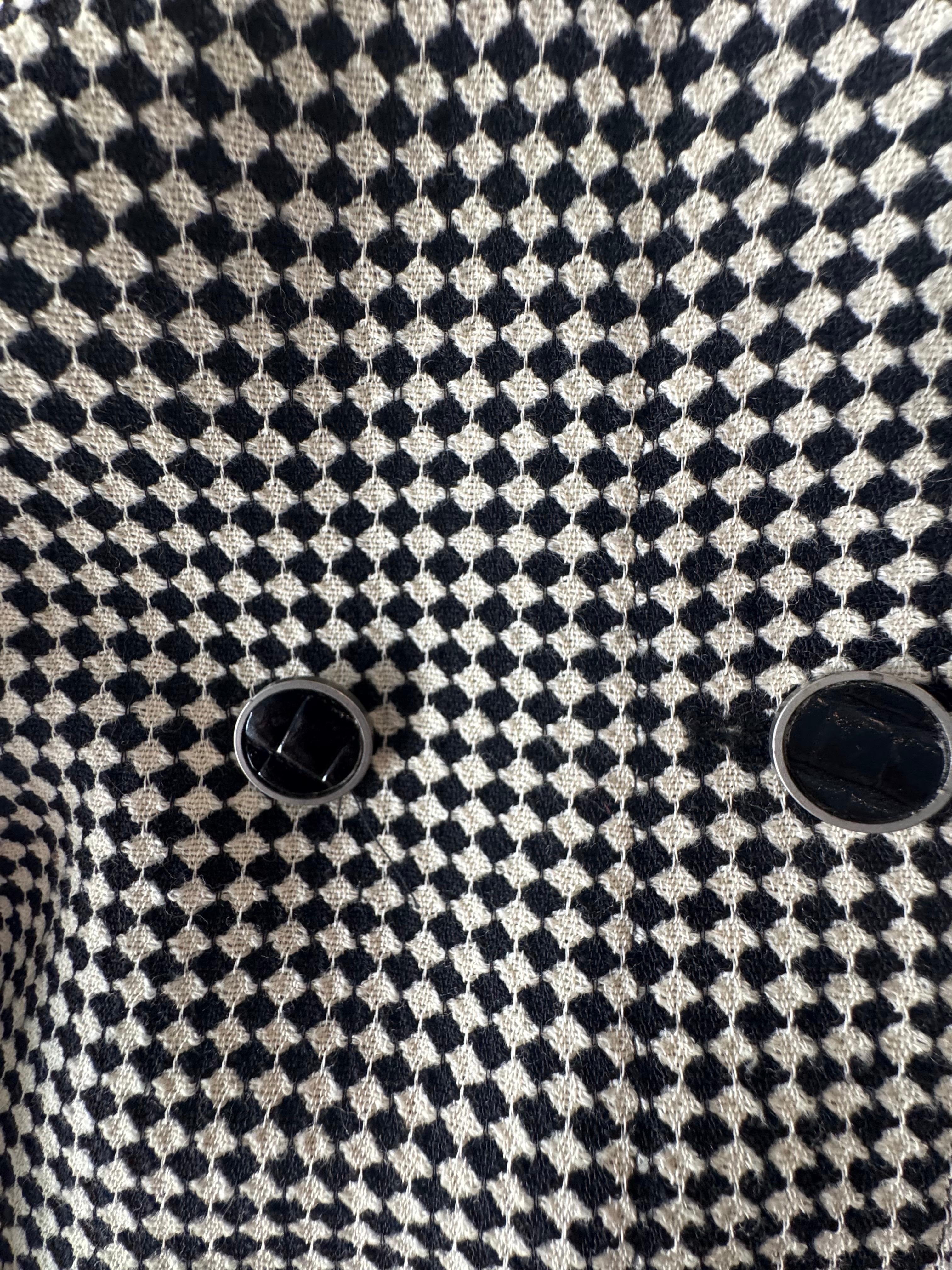 Gianni Versace ha creato una splendida sartoria per questo tailleur con gonna a quadri monocromatici.  La giacca è squadrata e presenta una chiusura asimmetrica con bottoni nascosti sul lato sinistro.  La mini gonna a matita è unica con un effetto a