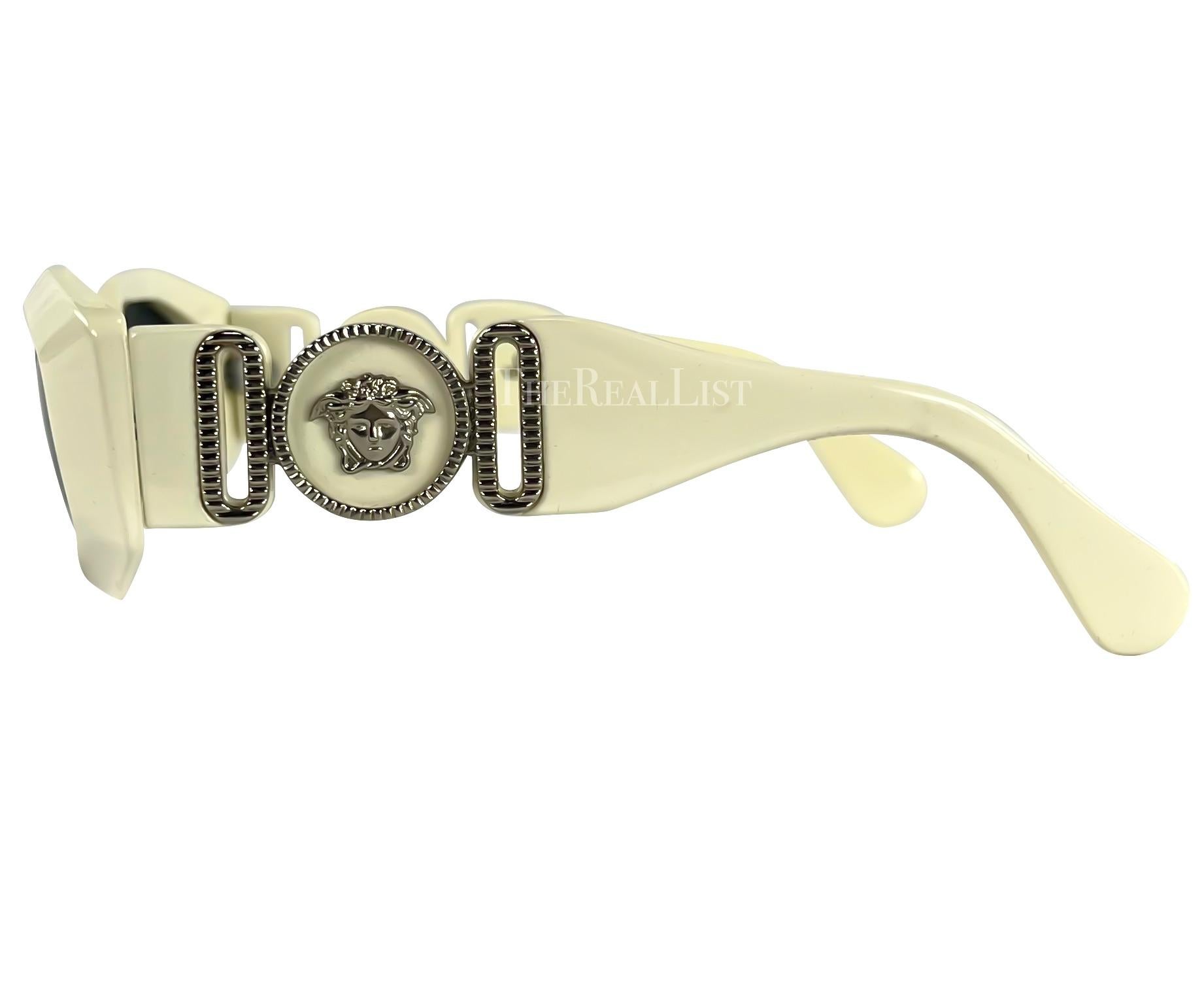 Presenting a pair of off-white Gianni Versace sunglasses. From the 1990s, these angular shades offer a fashionable nod to the iconic eyewear worn by rapper Biggie. The silver-tone metal accents on the arms highlight the Versace Medusa logo, adding a