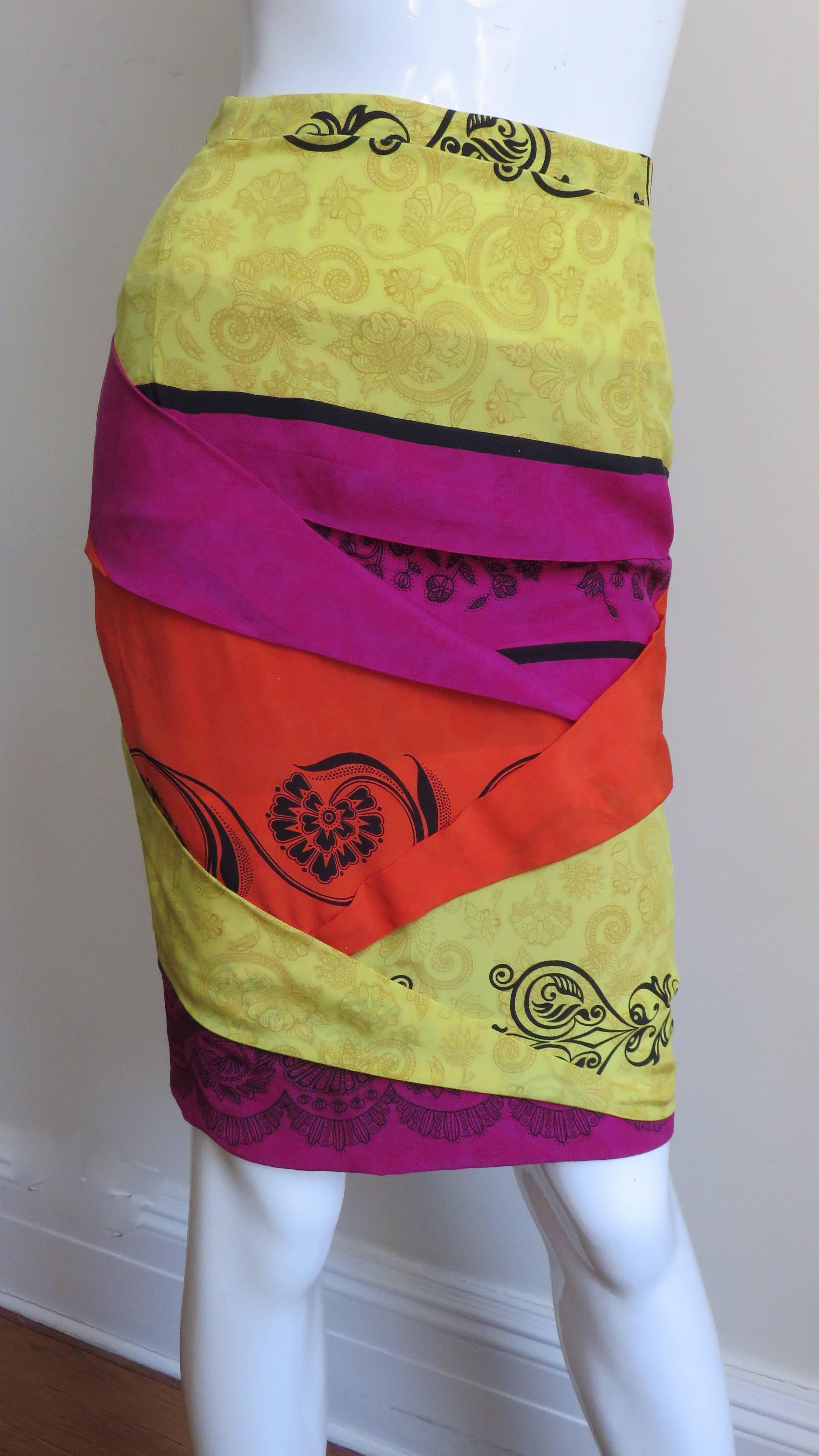 A fabulous silk skirt from Gianni Versace in yellow, orange and bright pink silk accented with a black abstract print. The skirt front and back has angled overlapping folds. It has a side zipper, a button at the waistband and matching pink