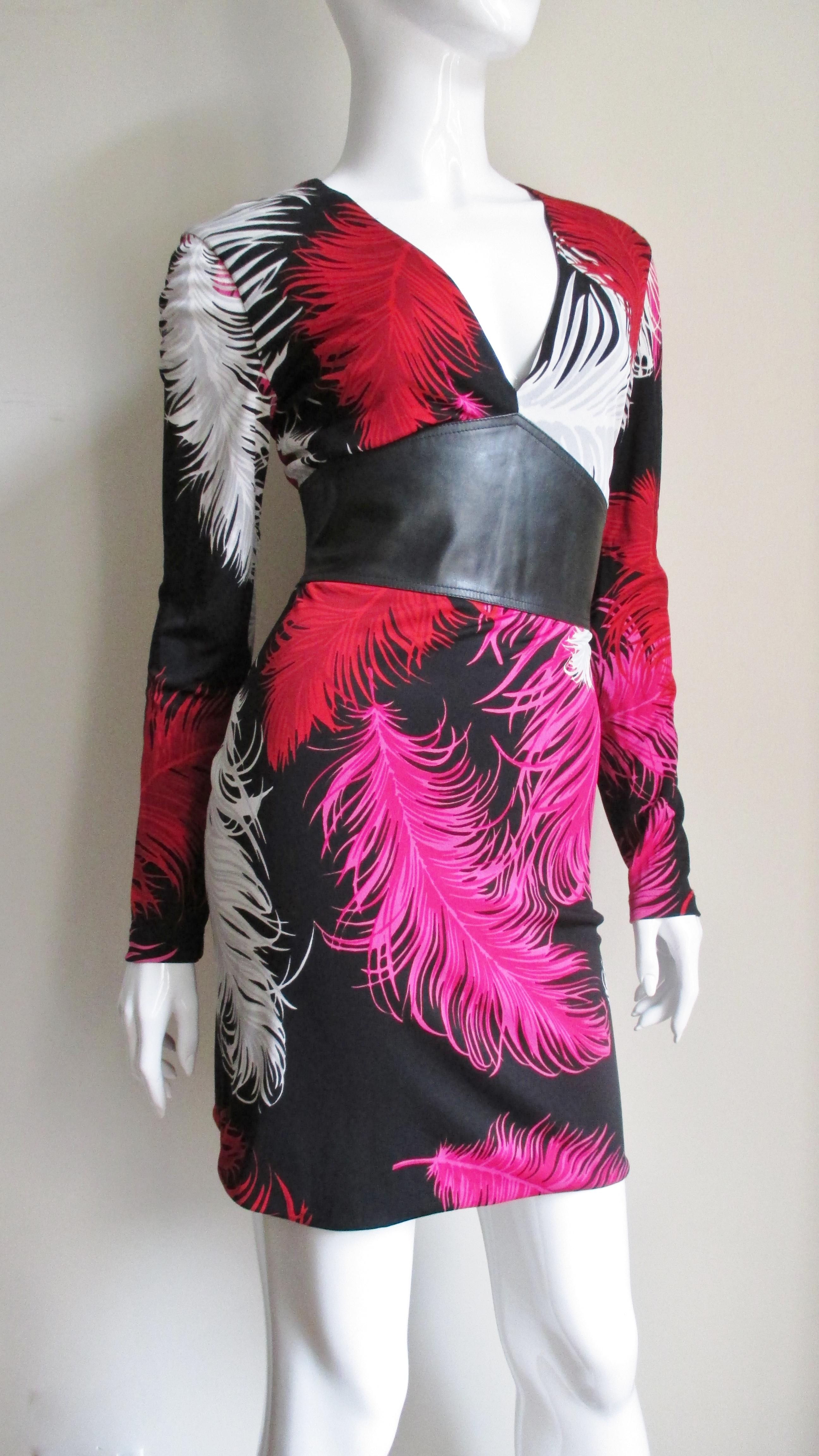 Une superbe robe en jersey de soie de Gianni Versace Couture dans un imprimé de plumes rose vif, rouge, blanc et gris sur noir.  Il a des manches longues et un décolleté en V qui rejoint un large empiècement en cuir noir autour de la taille qui se