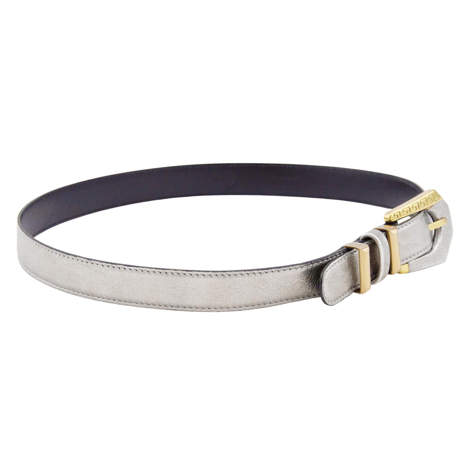 Gianni Versace thin waist belt from the early 1990s. Silver rigid leather with gold tone hardware. Gold on buckle features Greek key detailing. Belt loops are gold tone metal with a silver leather in between. Tonal silver top stitching. Black