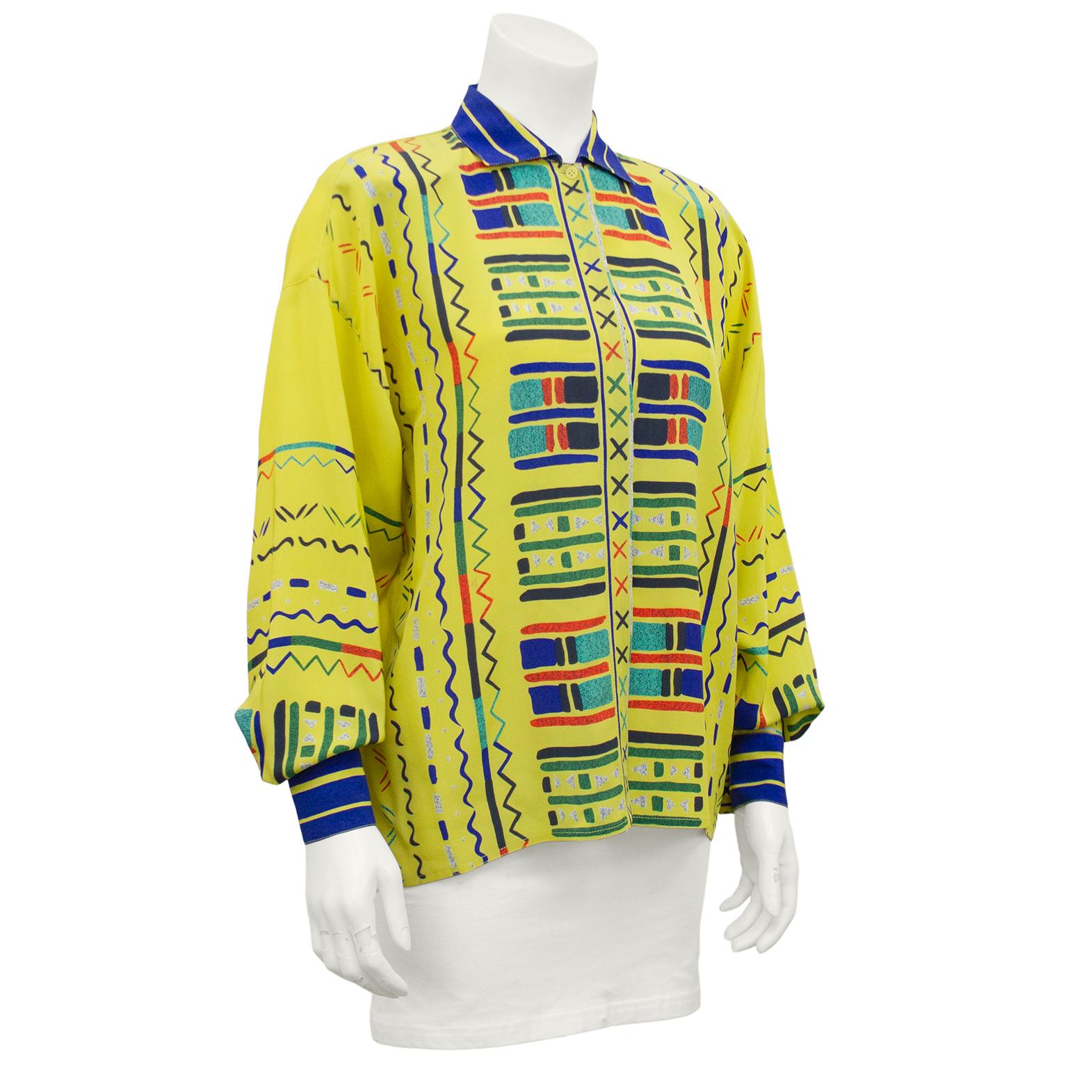 Gianni Versace silk blouse from the early 1990s. Highlighter yellow silk with multi colored geometric print all over the front and sleeves. Royal blue and yellow striped collar and cuffs. Bishop sleeves. Some minor speckling throughout which may be