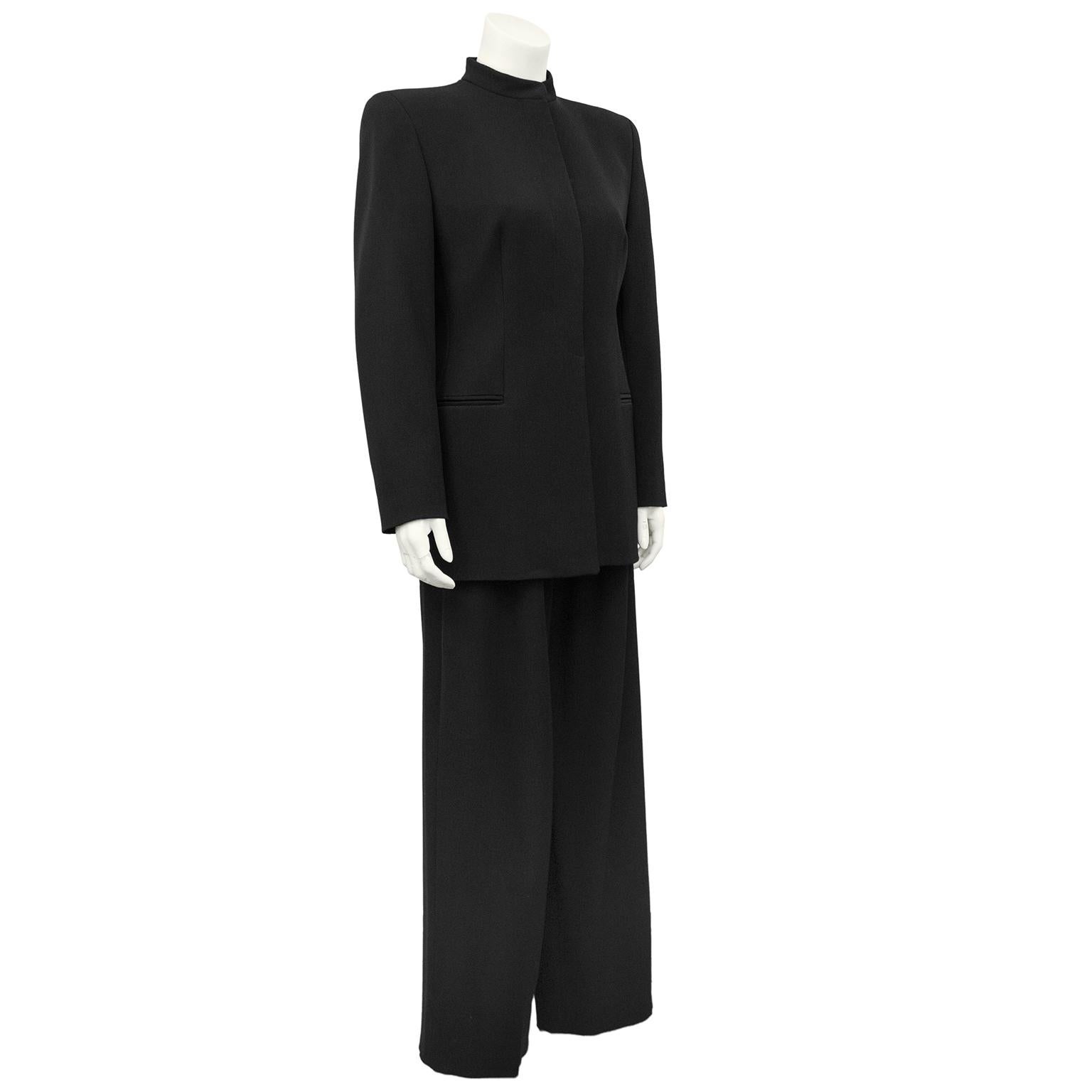 Beautiful and classic black silk crepe Giorgio Armani pantsuit. Jacket features a Mandarin collar, strong sharp shoulders, covered buttons and horizontal slit pockets. Jacket is long and hem hits below the hips. Trousers are high waisted with