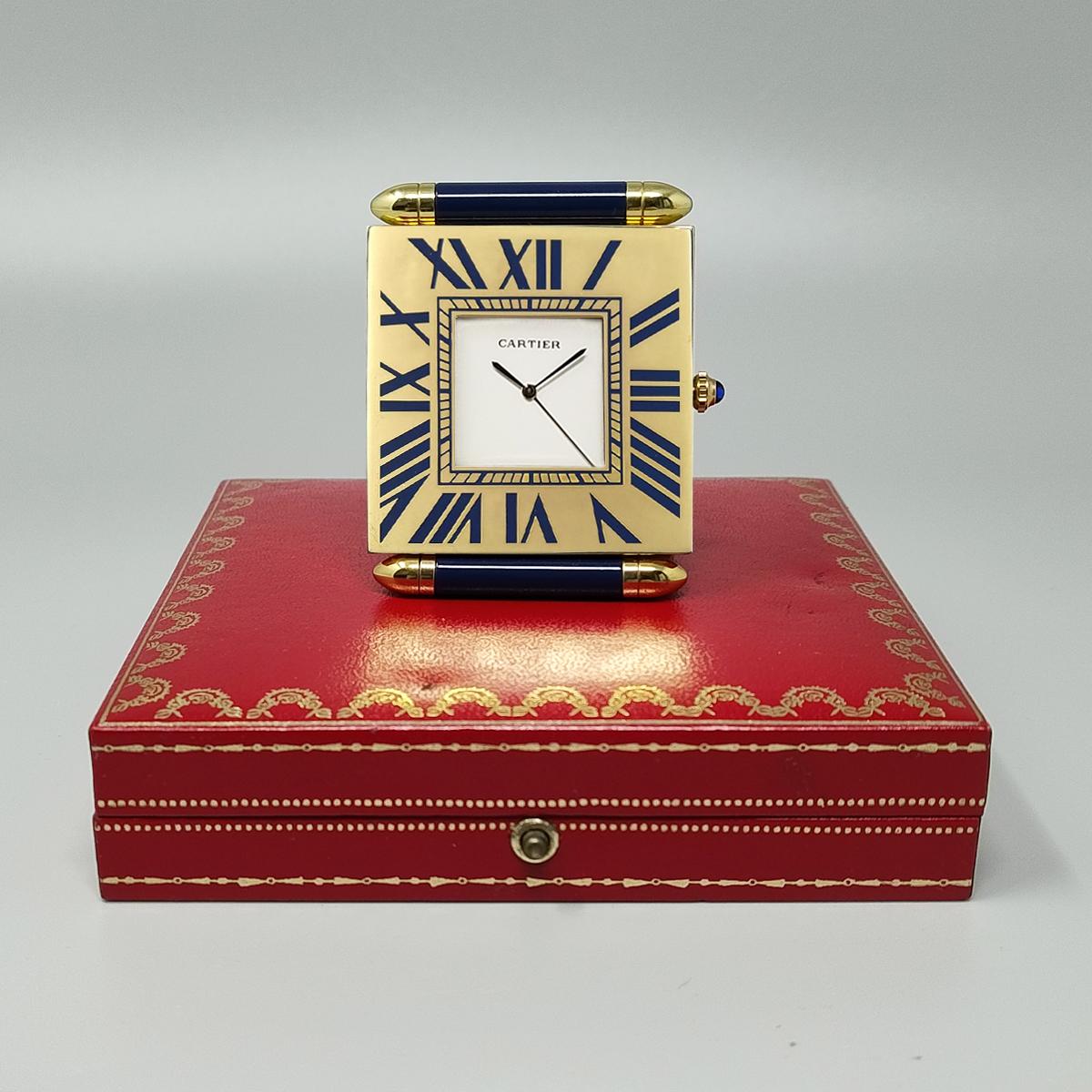 1990 Magnifique pendulette réveil Cartier avec cadran blanc en parfait état, aiguilles en acier, index romains sur monture plaquée or.  Fabriqué en Suisse.
Mouvement à quartz. Boîtier d'horloge numéroté 890905074. Avec étui d'origine et livret