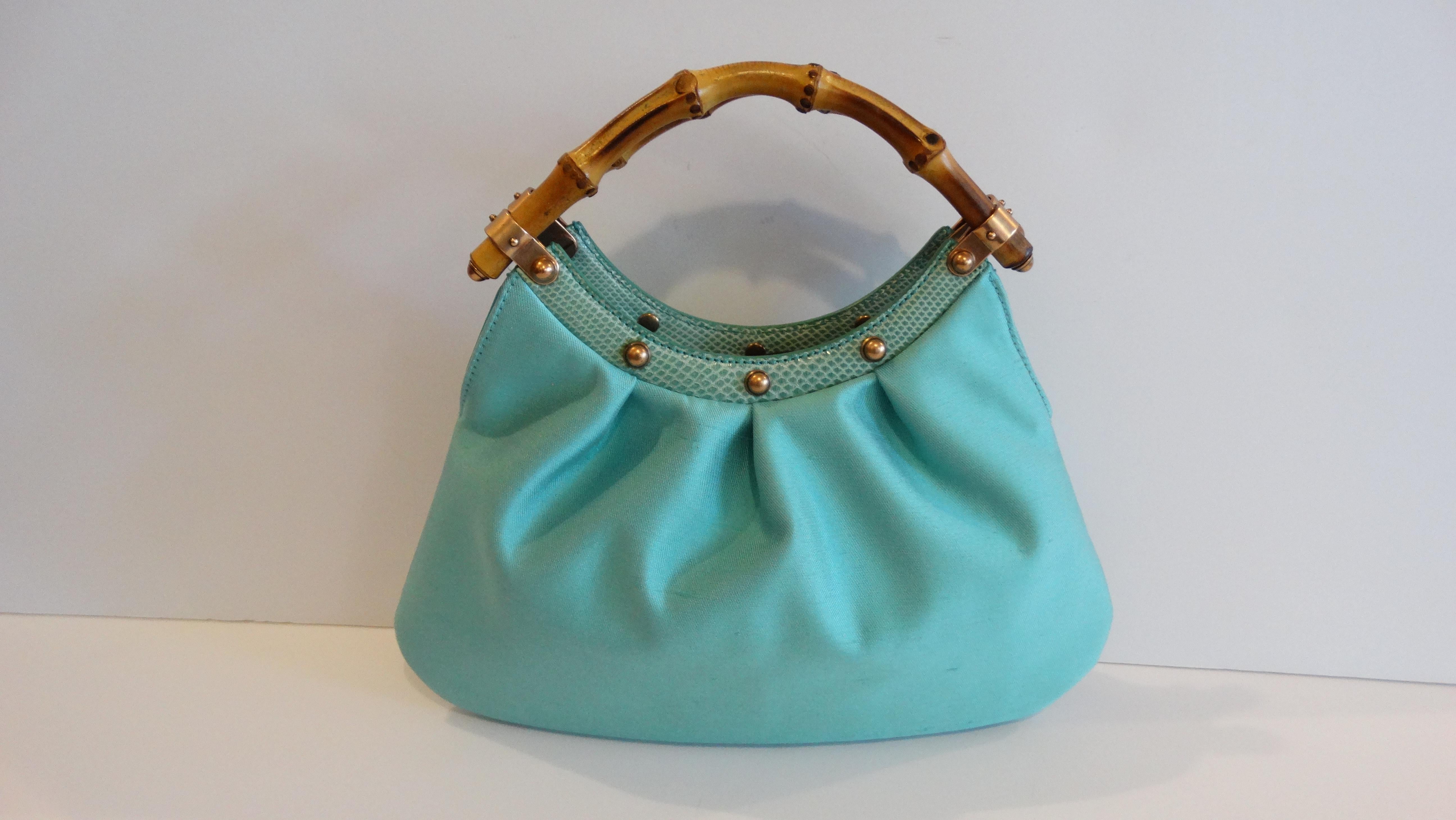 Get your Gucci on with this adorable handbag! Circa 1990s, this mini hobo bag is of made silk turquoise fabric and features beautiful dual bamboo handles. Includes gold-tone studded embellishments along the top of the tonal snake print accent.