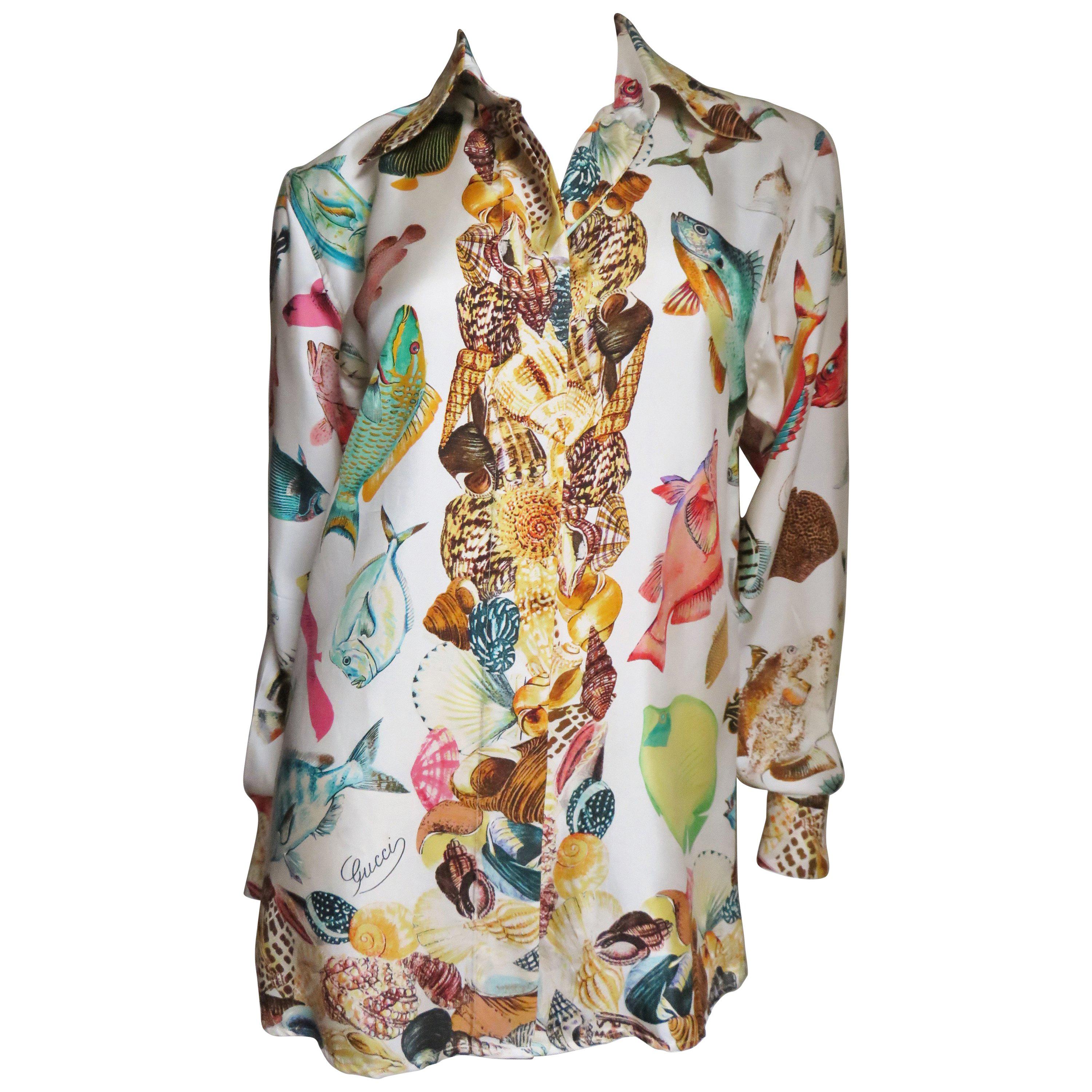 A beautiful off white silk shirt from Gucci with colorful fish pattern and shell pattern along the center front, cuffs and hemline.  It has a shirt collar, Gucci embossed mother of pearl buttons hidden in a front placket.   There is a gold metal