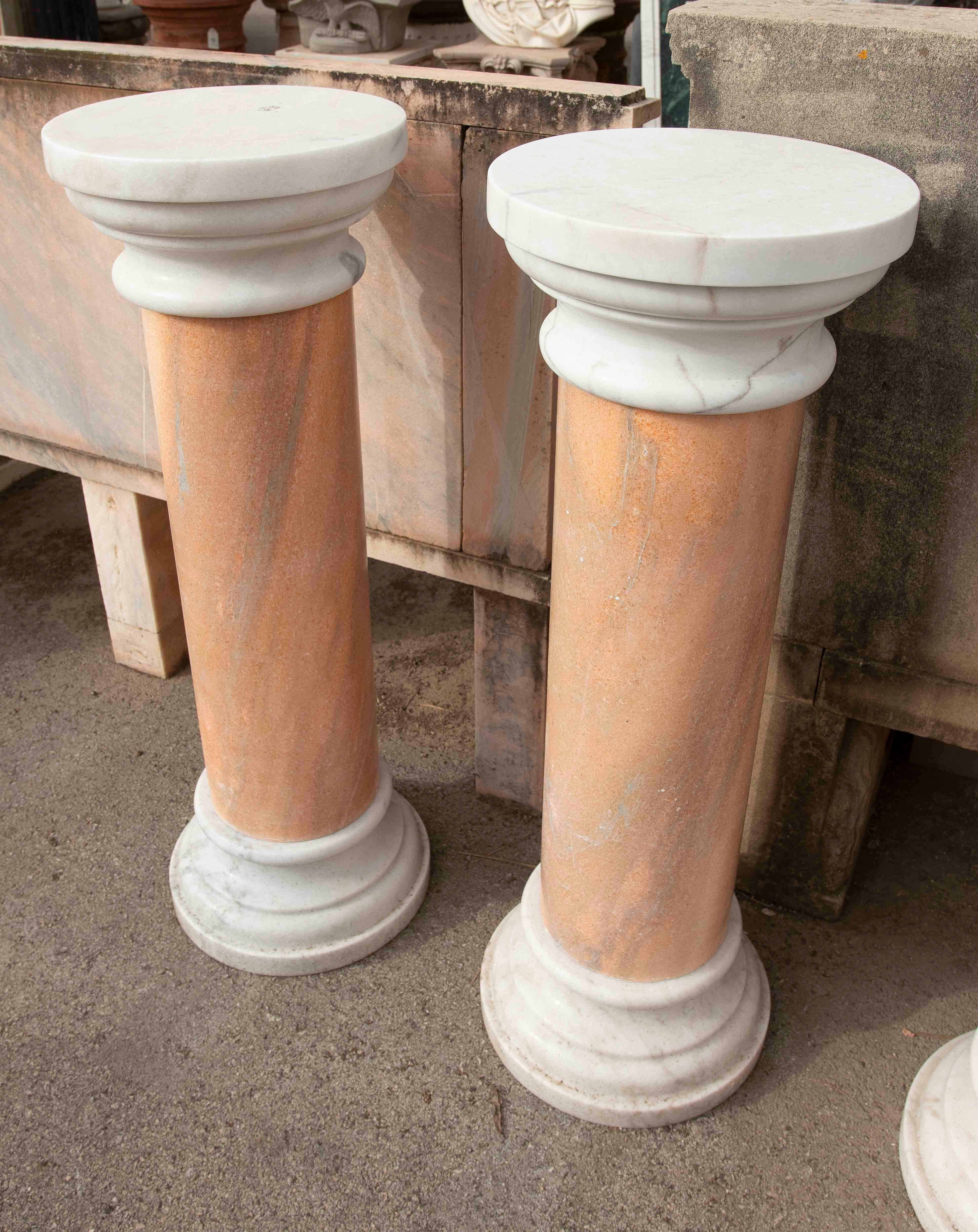 Ein elegantes Paar klassischer Säulen aus weißem und rosafarbenem Marmor, handgeschnitzt in einem zurückhaltenden und zeitlosen Design. Jede Säule hat einen zylindrischen Schaft aus rosafarbenem Marmor mit weicher, natürlicher Maserung und Endstücke