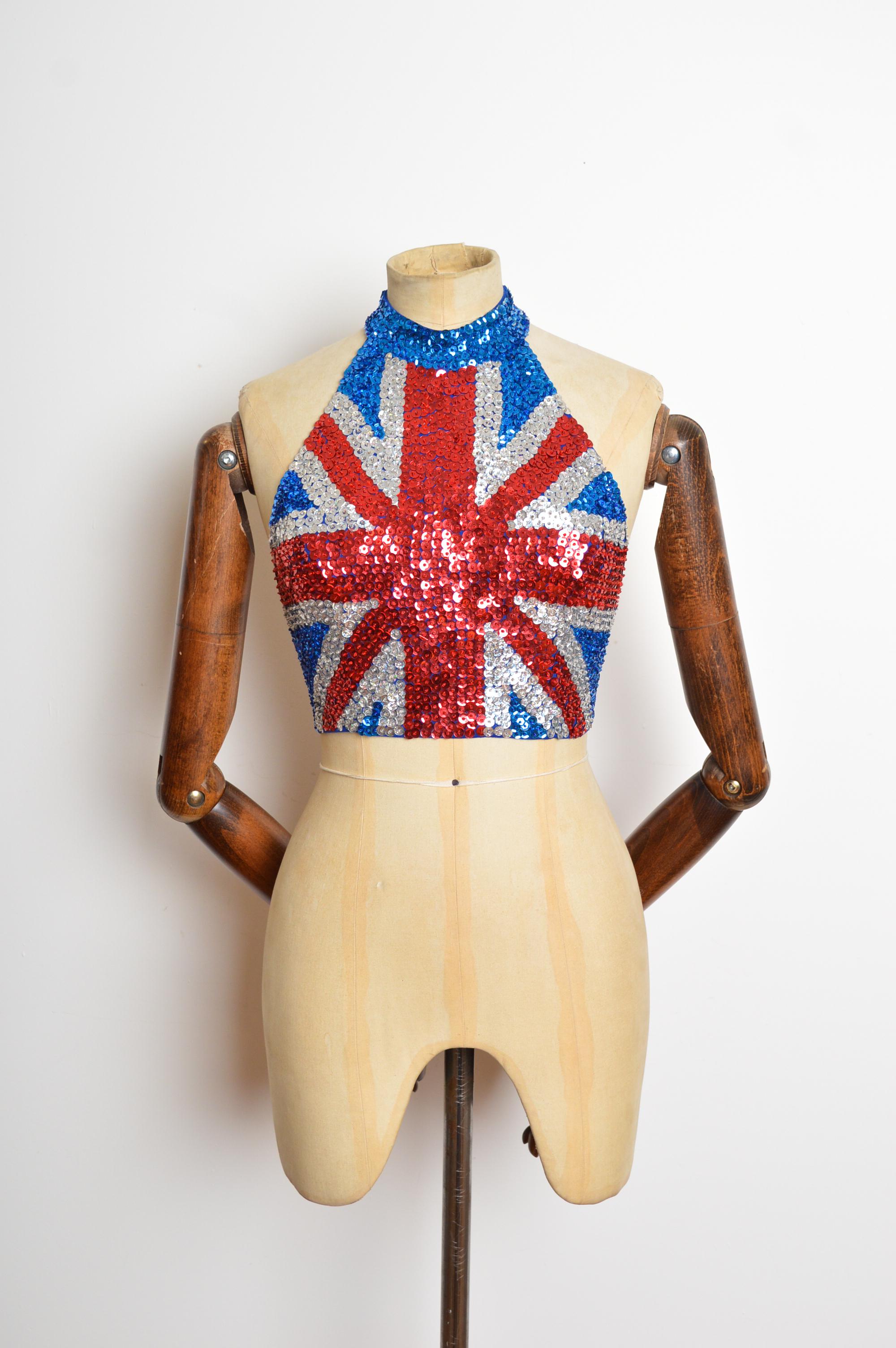 Un divertido top hecho a mano con la Union Jack de lentejuelas de los años 90. Con lentejuelas y abalorios cosidos a mano, cuello con cierre de velcro seguro y gancho de herrador en la espalda. 
Las medidas se indican en pulgadas ('')
Talla