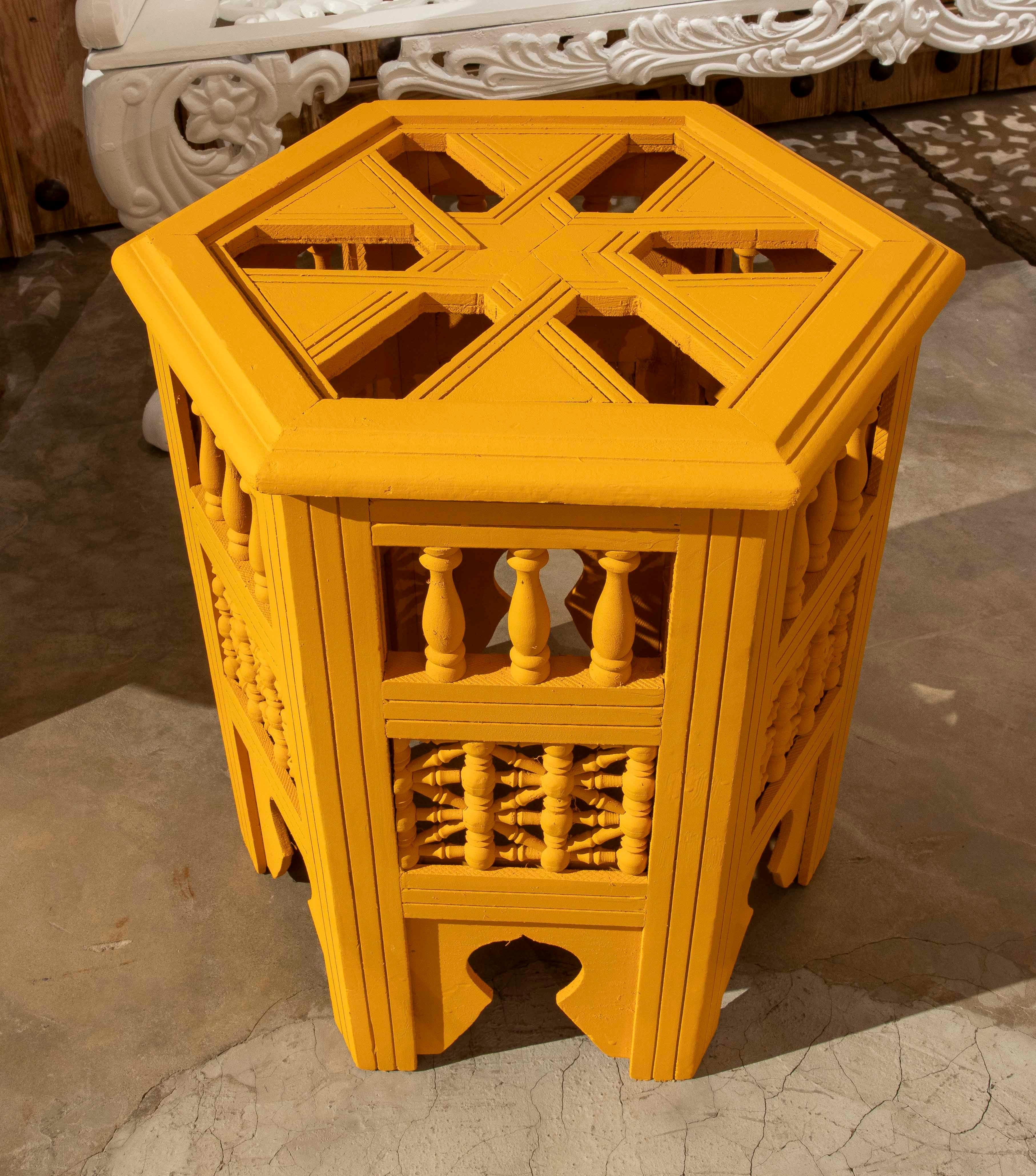 This handcrafted hexagonal table is a distinctive piece of traditional design reinterpreted with a vibrant contemporary finish. Made of carved wood, it features turned details on the sides with small columns and decorative weaving, giving it an air