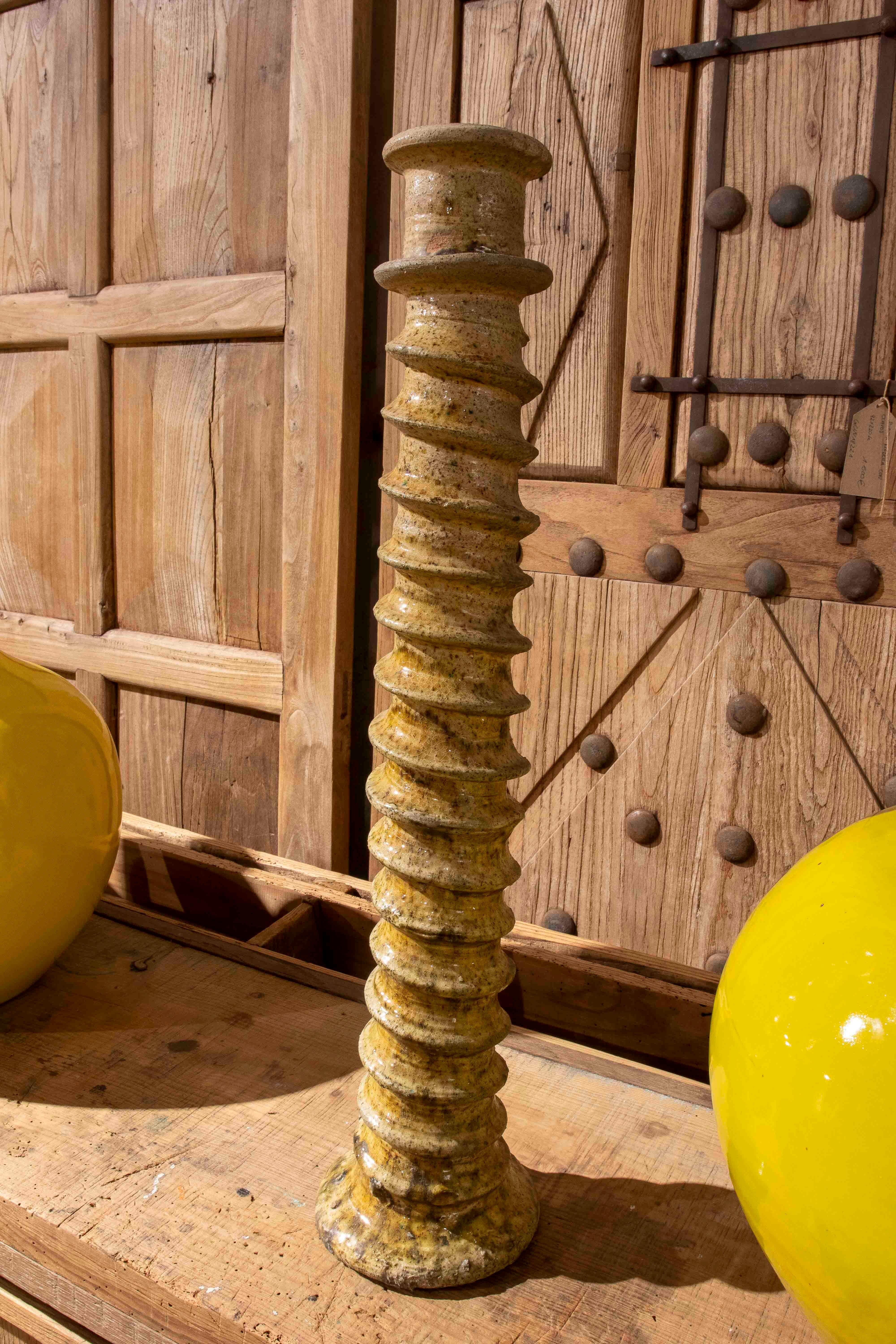 Candelabro marmoreo in ceramica lavorata in un'accattivante tonalità amarillo, caratterizzato da una forma ascendente a spirale e da un rivestimento artistico. Il pezzo mostra un aspetto irregolare proprio della produzione manuale tradizionale, con