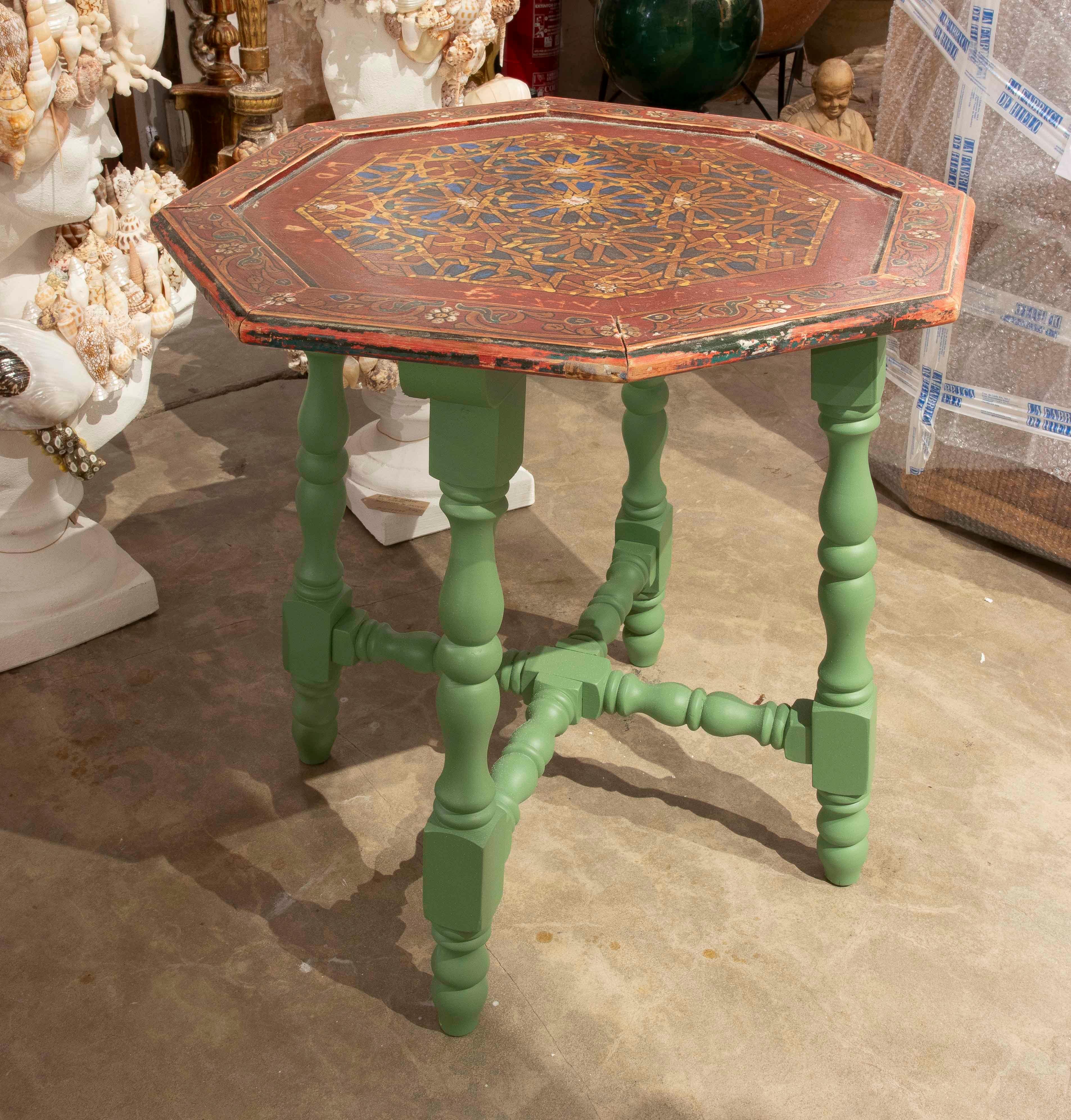 Descubre esta mesa auxiliar octogonal hecha a mano, una pieza única que combina tradición y estilo contemporáneo. Su base de madera torneada está pintada en un elegante verde mate, que resalta la silueta clásica de las patas con un aire fresco y