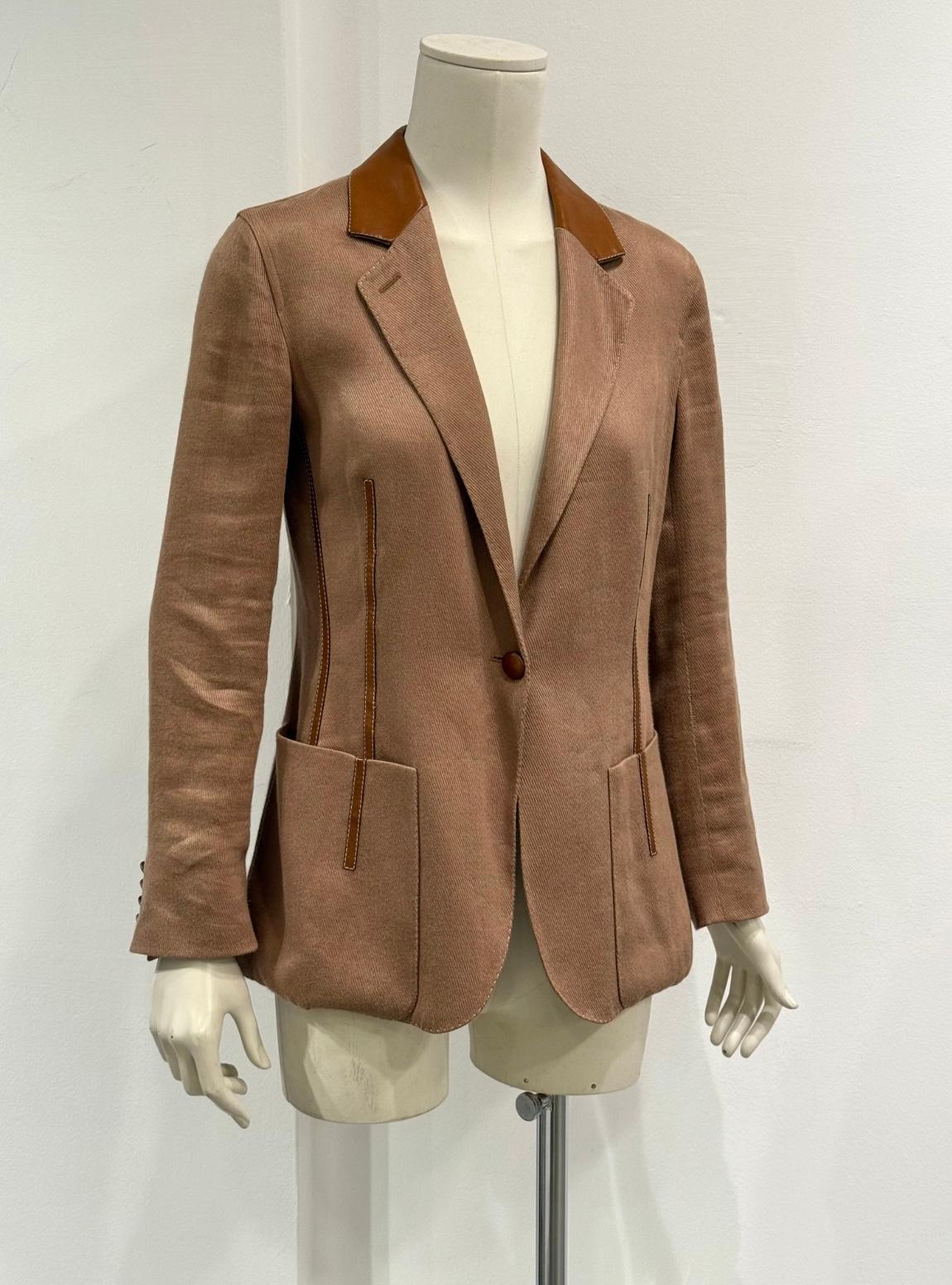Este blazer Hermès de los años 90 es una refinada expresión de elegancia de inspiración ecuestre. Confeccionado en una cálida mezcla de lana color arena, presenta lujosos detalles de piel caramelo en el cuello y los bolsillos, que combinan suavidad