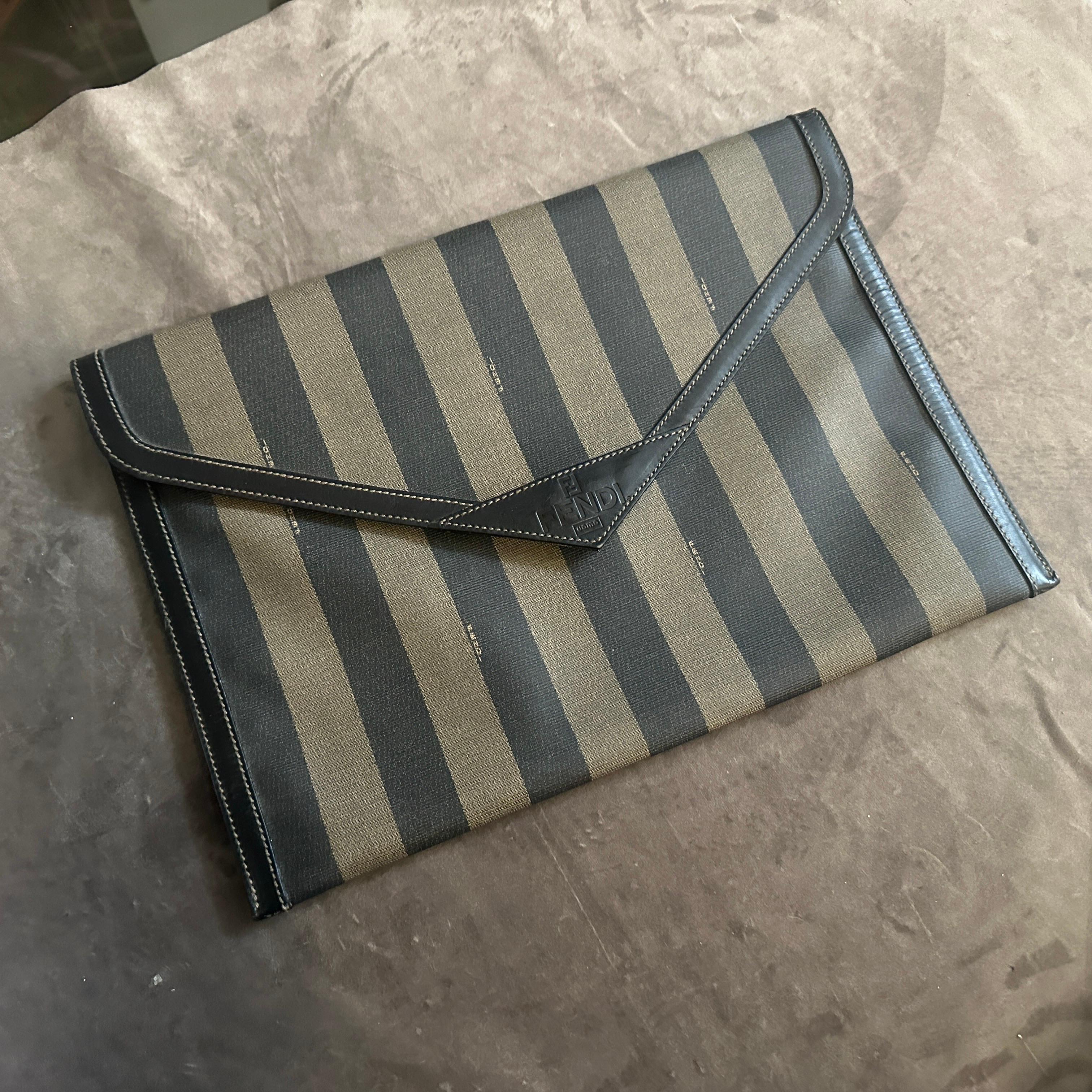 This is a truly iconic piece of vintage luxury: an authentic Fendi clutch from the 1990s. The bag features Fendi’s signature Pequin striped canvas, a classic, instantly recognizable non-logo logo motif launched in 1983 by Karl Lagerfeld and the