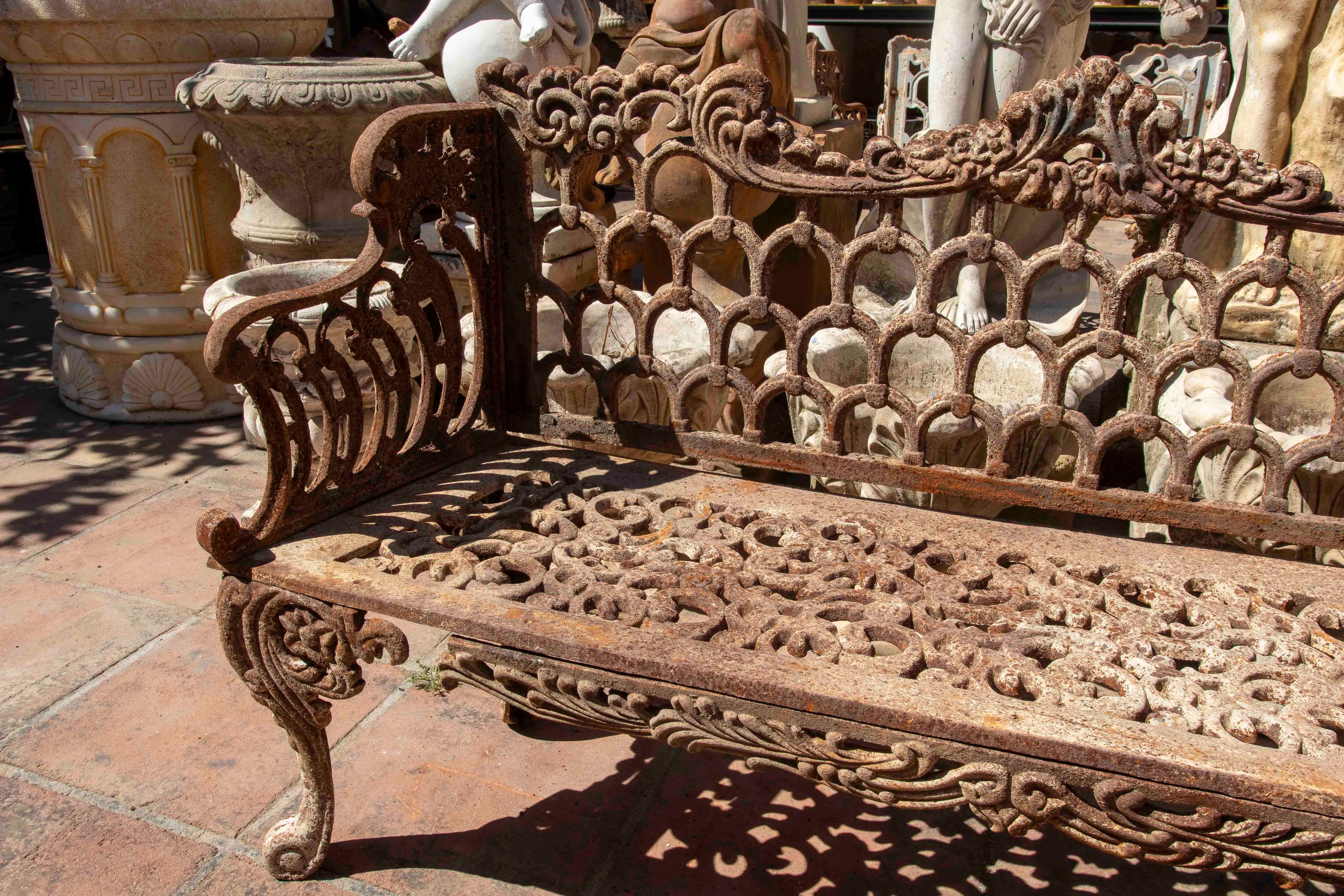 Panchina da giardino in ferro con schienale traforato con un disegno intrecciato a forma di archi gotici e motivi floreali. La seduta e le gambe presentano rilievi decorativi a forma di volute e fogliame, caratteristici dello stile vittoriano. Il