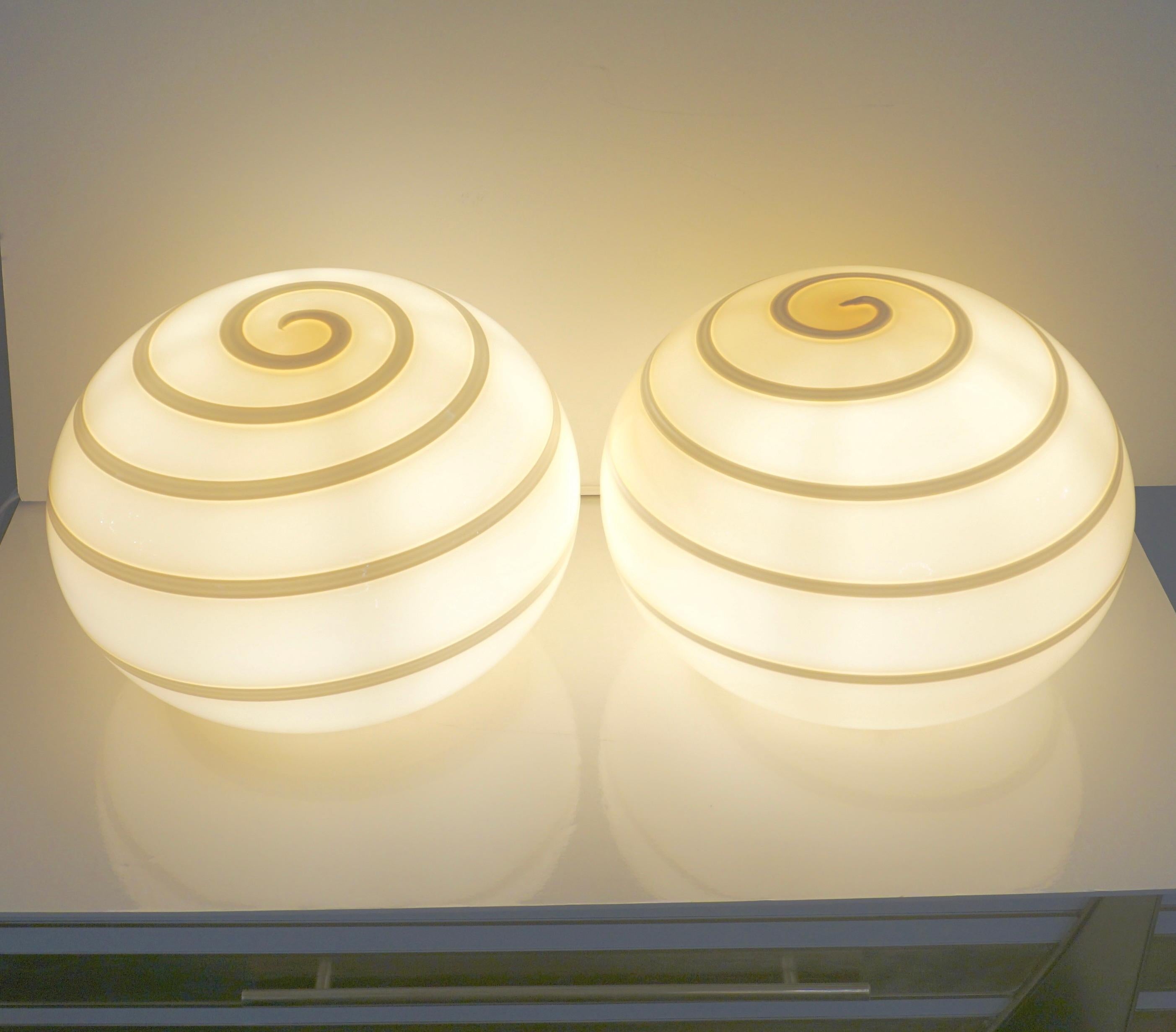 Do you miss the 1970s Design Style? So these are for you! A minimalist pair of late 20th Century Italian blown ivory buttercream glass lamps, of simple oval shape with a geometric swirl pattern of white spiraling Murrina. The glass shade rests on an