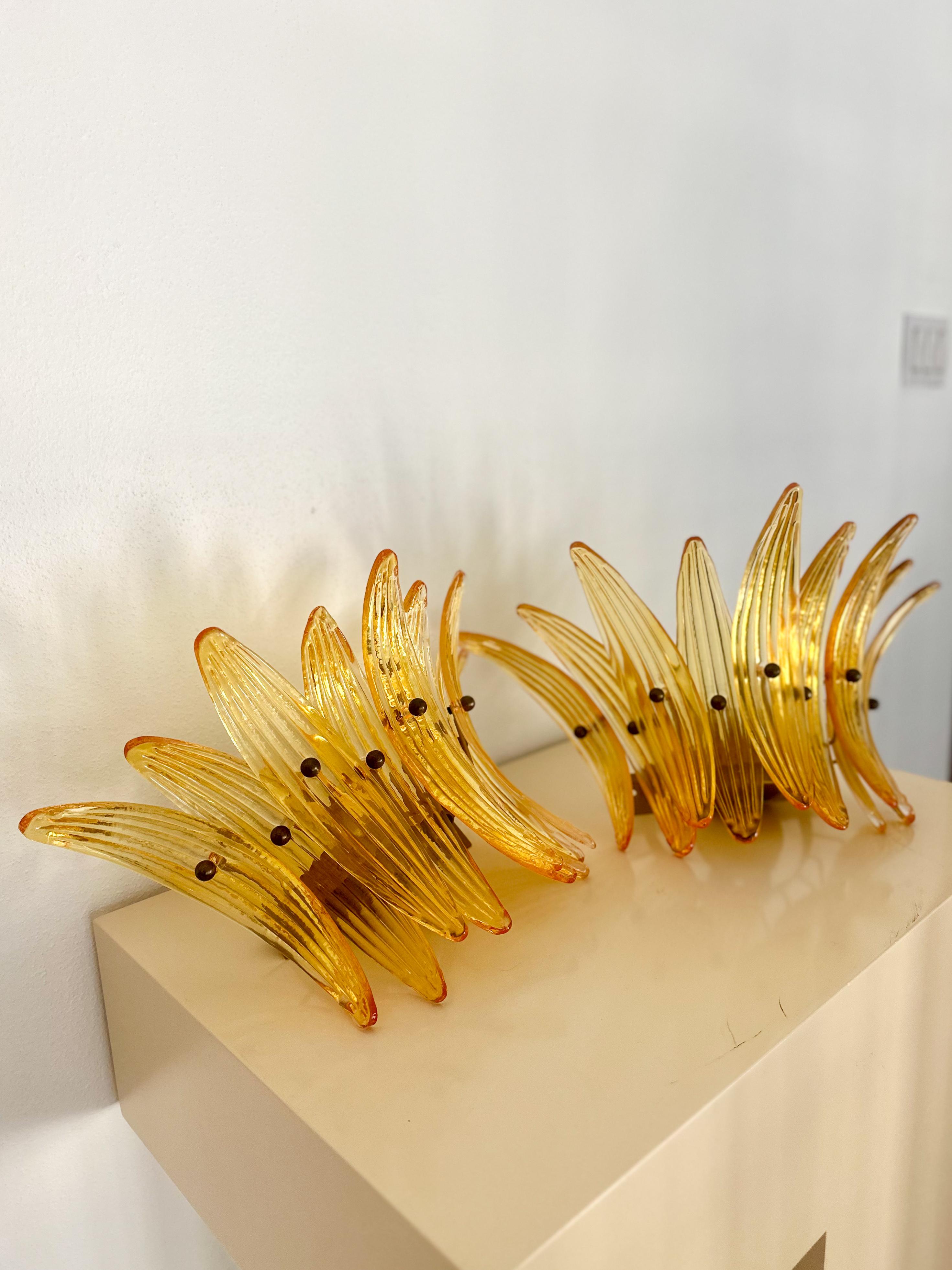 Atemberaubende Wandleuchten aus mundgeblasenem Murano-Glas, ca. 1990er Jahre. Jede Leuchte verfügt über 9 konkave Applikationen aus bernsteinfarbenem, geriffeltem Glas, die mit Messingbeschlägen in einem Palmenmuster am Rahmen befestigt sind. Farbe