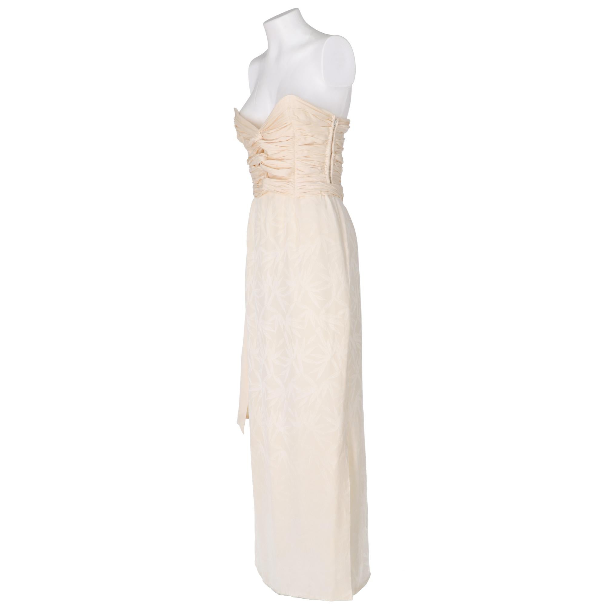 Ivory tailored wedding dress, with straight long skirt up to the feet in jacquard fabric with floral motif, heart neckline and top with curled and knotted fabric, decorative belt, zip closure on the side.

Years: 1990s

Size: 42 IT

Linear