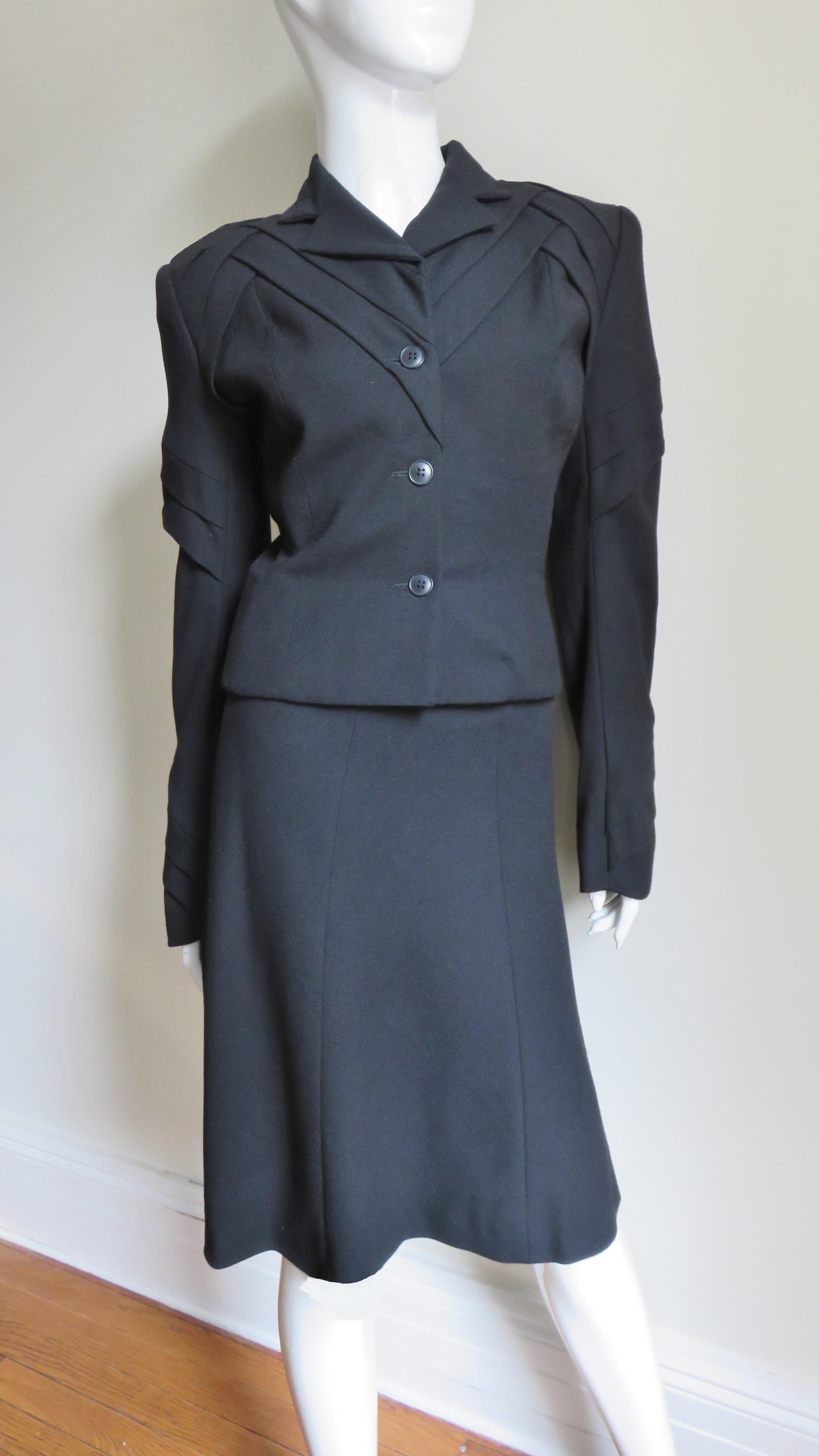 A gorgeous black wool suit with a twist by John Galliano.  It consist of a hip length single breasted jacket with small lapels and beautiful detail at the upper jacket including the sleeves creating fabulous angles and lines.  The matching 6 panel