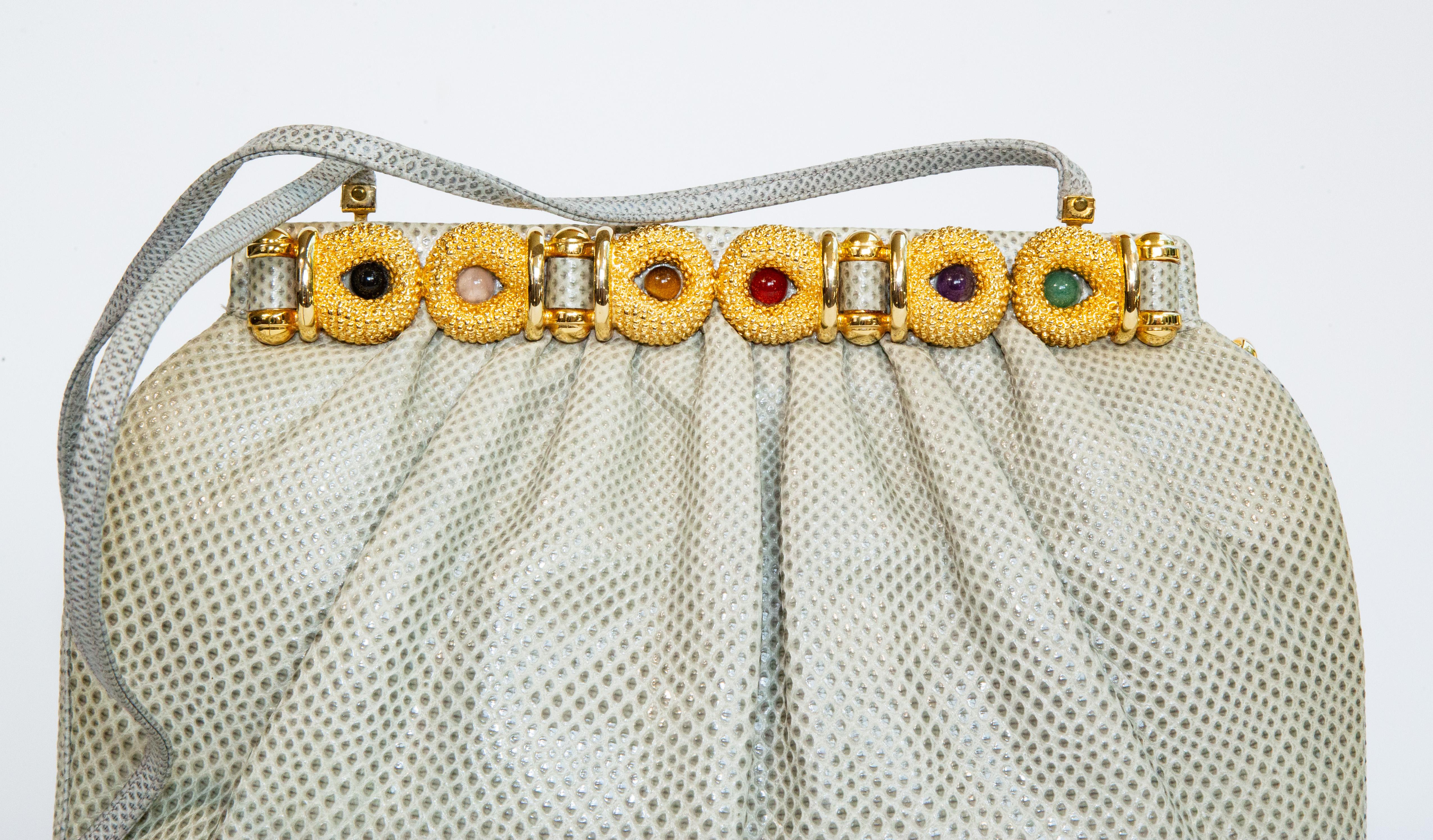 Sac à bandoulière/clutch de soirée en peau de lézard avec des pierres précieuses serties dans des ferrures dorées. La bandoulière mesure 100 cm de long et peut être placée à l'intérieur du sac pour l'utiliser comme une pochette. L'intérieur est