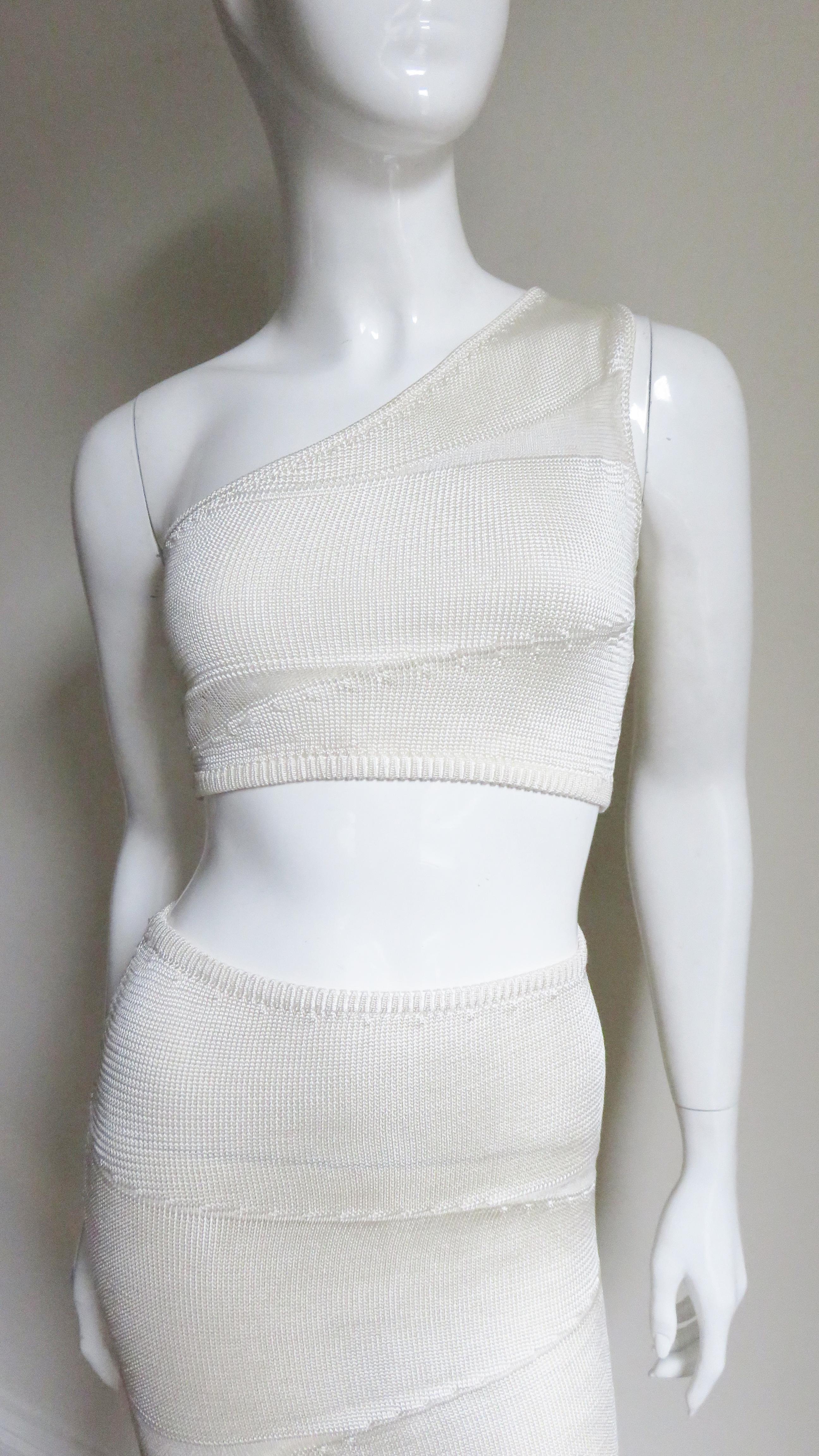 This is a fabulous 2 piece white silk knit skirt and crop top set from Krizia.  The one shoulder crop top has fine wedges of mesh covered sheer paneling angled above and below the bust line and on the pencil skirt on an otherwise solid white silk