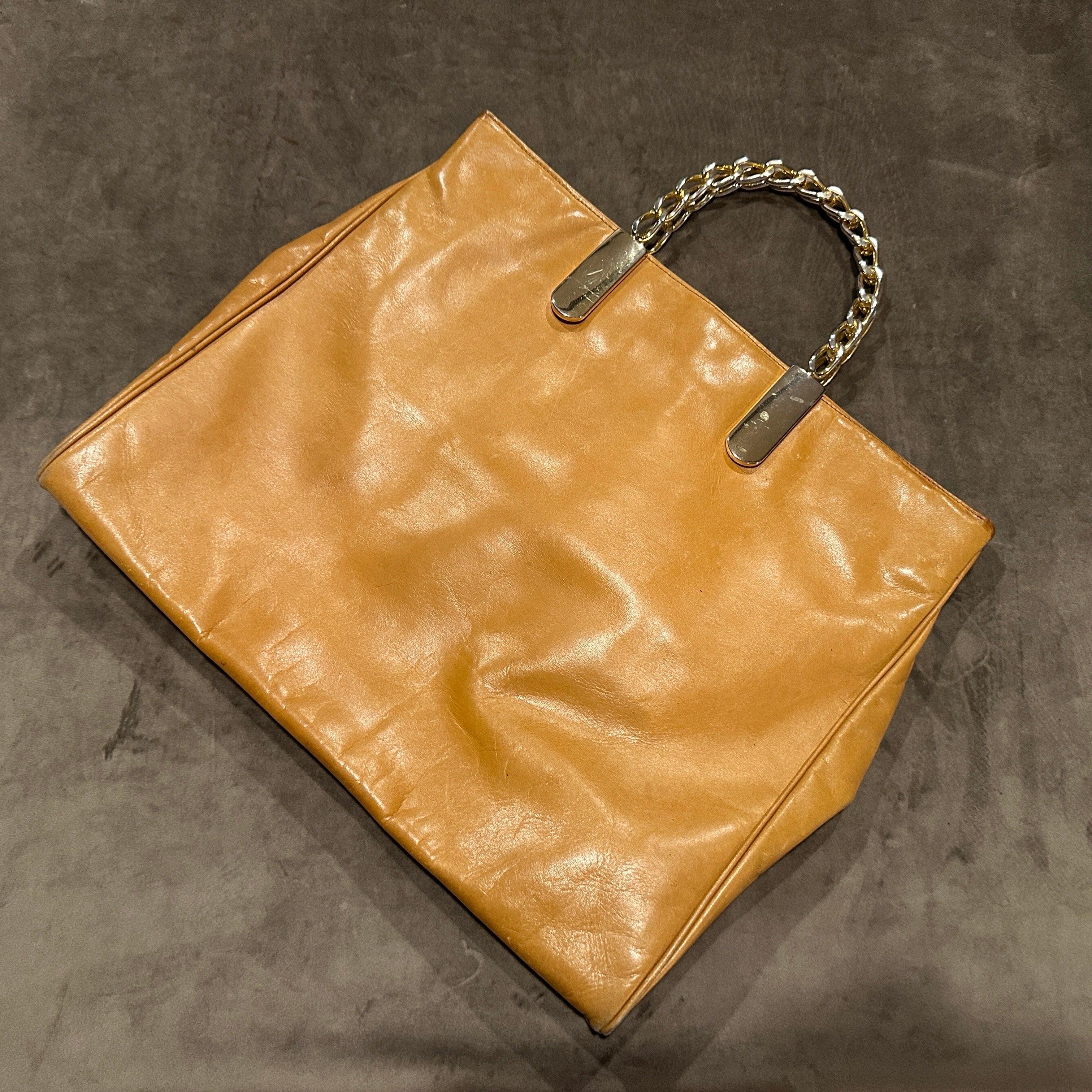 This is a vintage Italian tote bag by Edoardo Giannotti from the 1990s, featuring a generous rectangular shape crafted from high-quality light tan eather and distinguished by striking gilded metal chain link handles anchored by shiny metal plaques,
