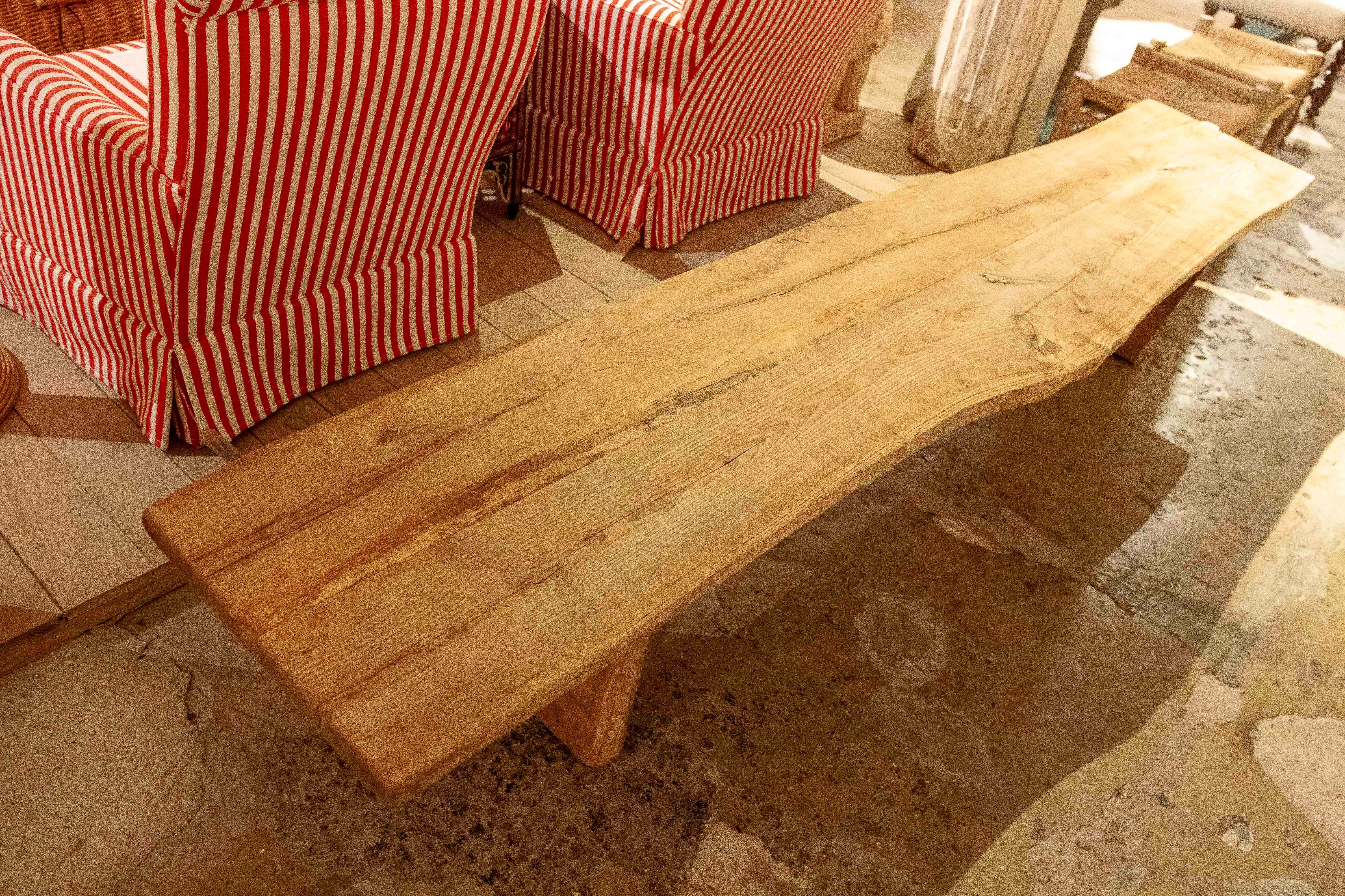 Grand banc rustique en bois massif, au design simple et fonctionnel qui met en valeur la beauté naturelle du matériau. Son plateau conserve la forme organique du bois, avec des veines et des nœuds visibles qui confèrent authenticité et caractère à