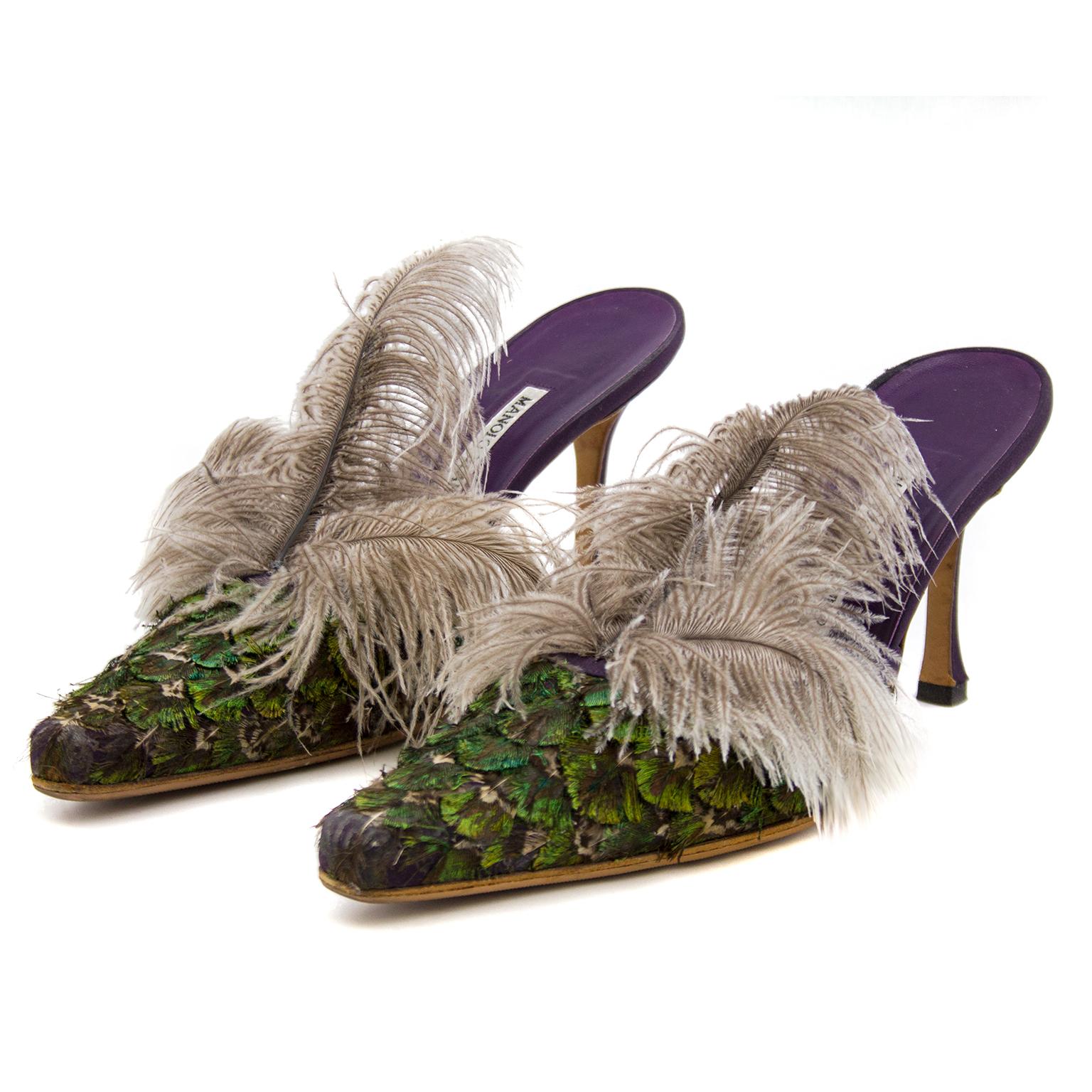 Birds of a feather! These Manolo Blahnik high heeled mules look like a pair of exotic birds for your feet. The pointed toe box is covered in iridescent green and purple feathers in an overlapping formation and finished with a plume of 3 grey long