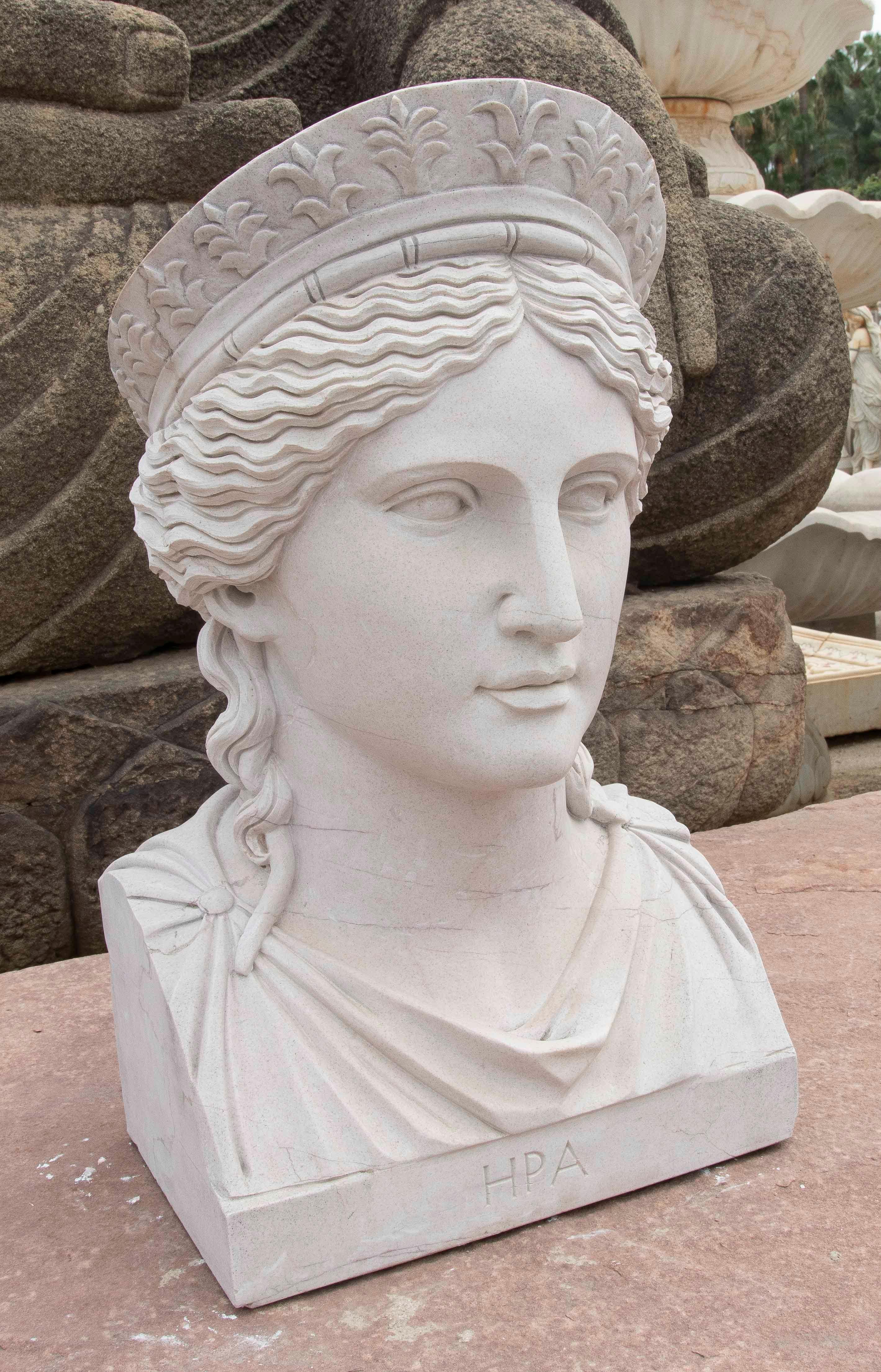 Exquisito busto de mármol que representa a Hera, la diosa griega del matrimonio y la realeza, reconocible por su delicado tocado coronado con motivos vegetales. Finamente tallado, muestra un rostro sereno y detallado, con rasgos armoniosos y