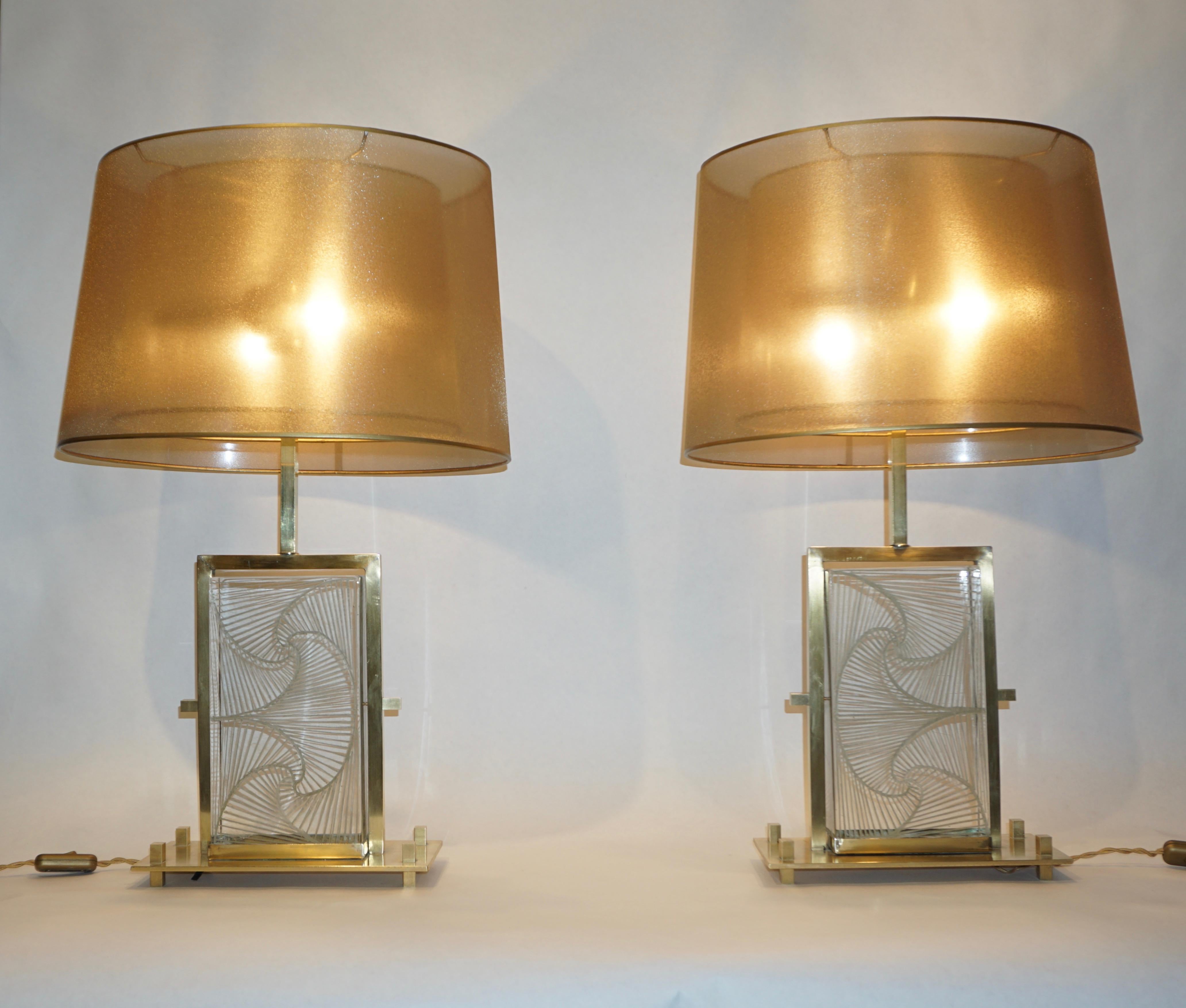 1990s pair of architectural table lamps, entirely handcrafted. The geometric body composed of a thick rock crystal Murano glass block is engraved with floral calla lily motif with gold reflections, floating in a slim urban design brass structure and