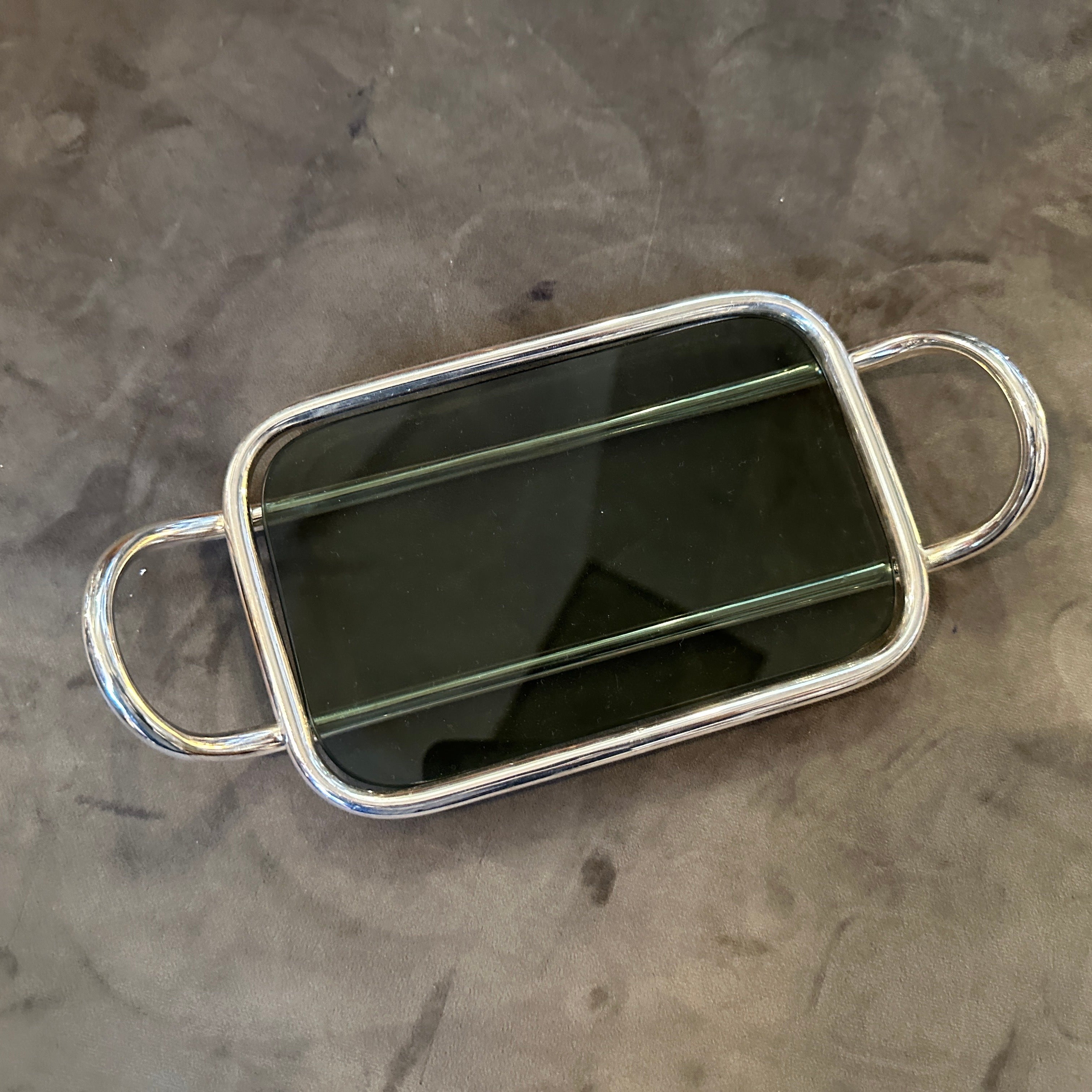 Dieses modernistische Buttertablett von Lino Sabattini aus den 1990er Jahren verkörpert die minimalistische und raffinierte Ästhetik des Designers, mit klaren Linien und hochwertigen Materialien. Der Sockel dieses Tabletts ist aus dunkelgrauem Glas
