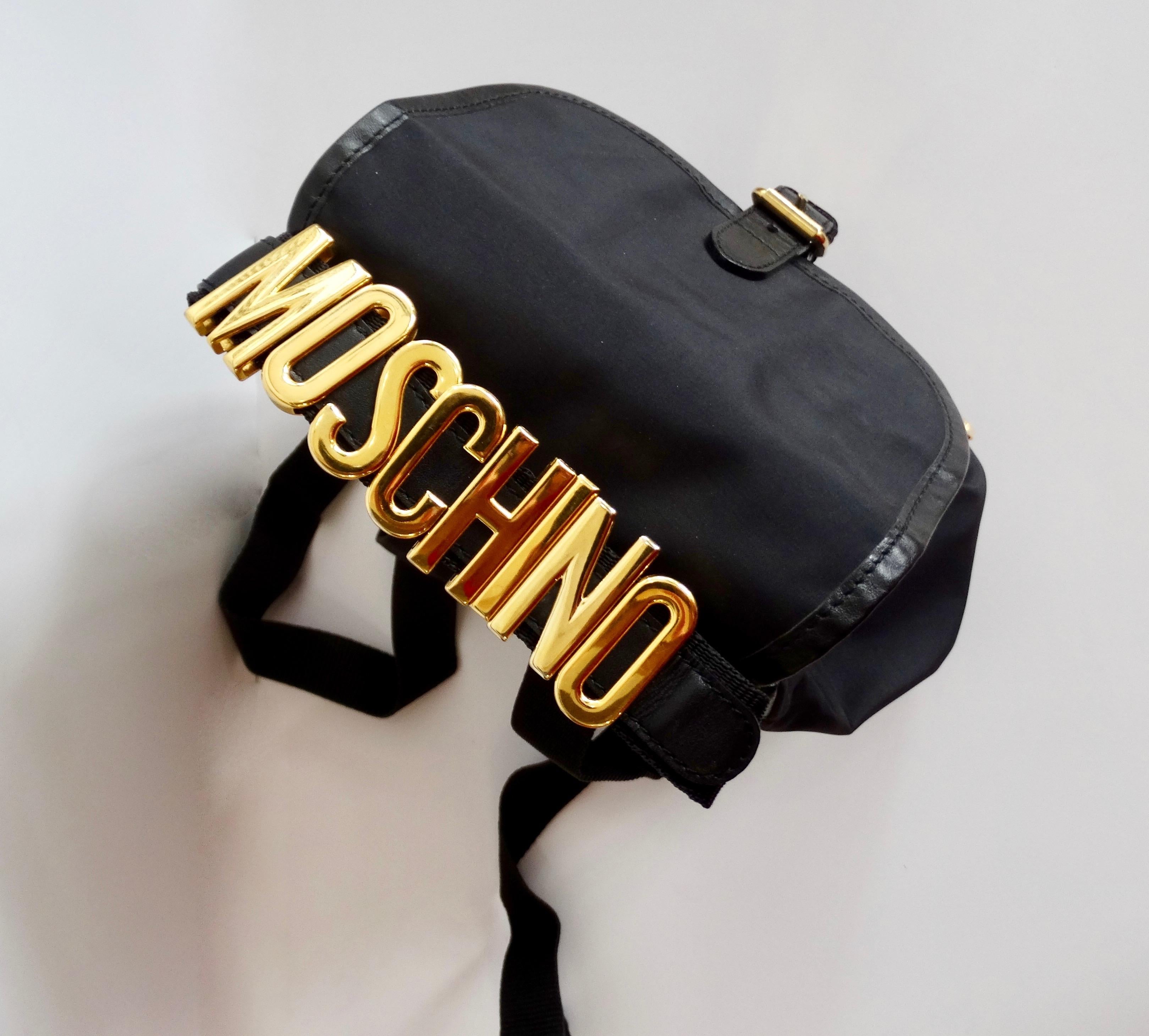 Always be ready to go with this adorable Moschino backpack! Circa 1990s, this mini black nylon drawstring backpack includes a black leather trim and gold toned hardware. Features a belt style front flap closure, adjustable straps and an exterior