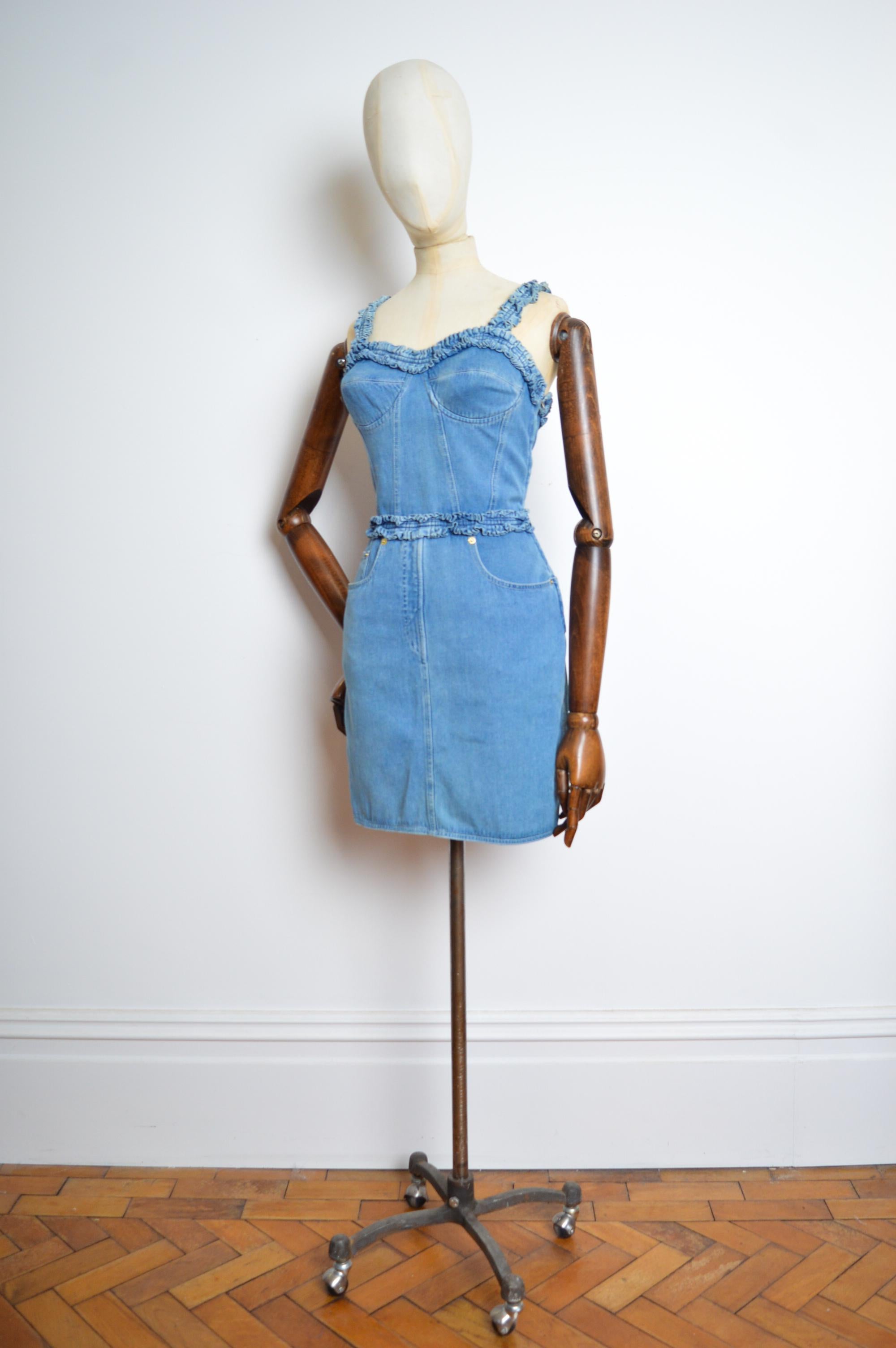 Mid blue denim Moschino dress circa 1990 featuring ruffled strappy shoulders, figure hugging shape, concealed side zip and classic 4 pocket design.
Pit to Pit; 30” under the bust. 
Top of shoulder to Hem; 36”
Waist; 26”
Size; Small (we would