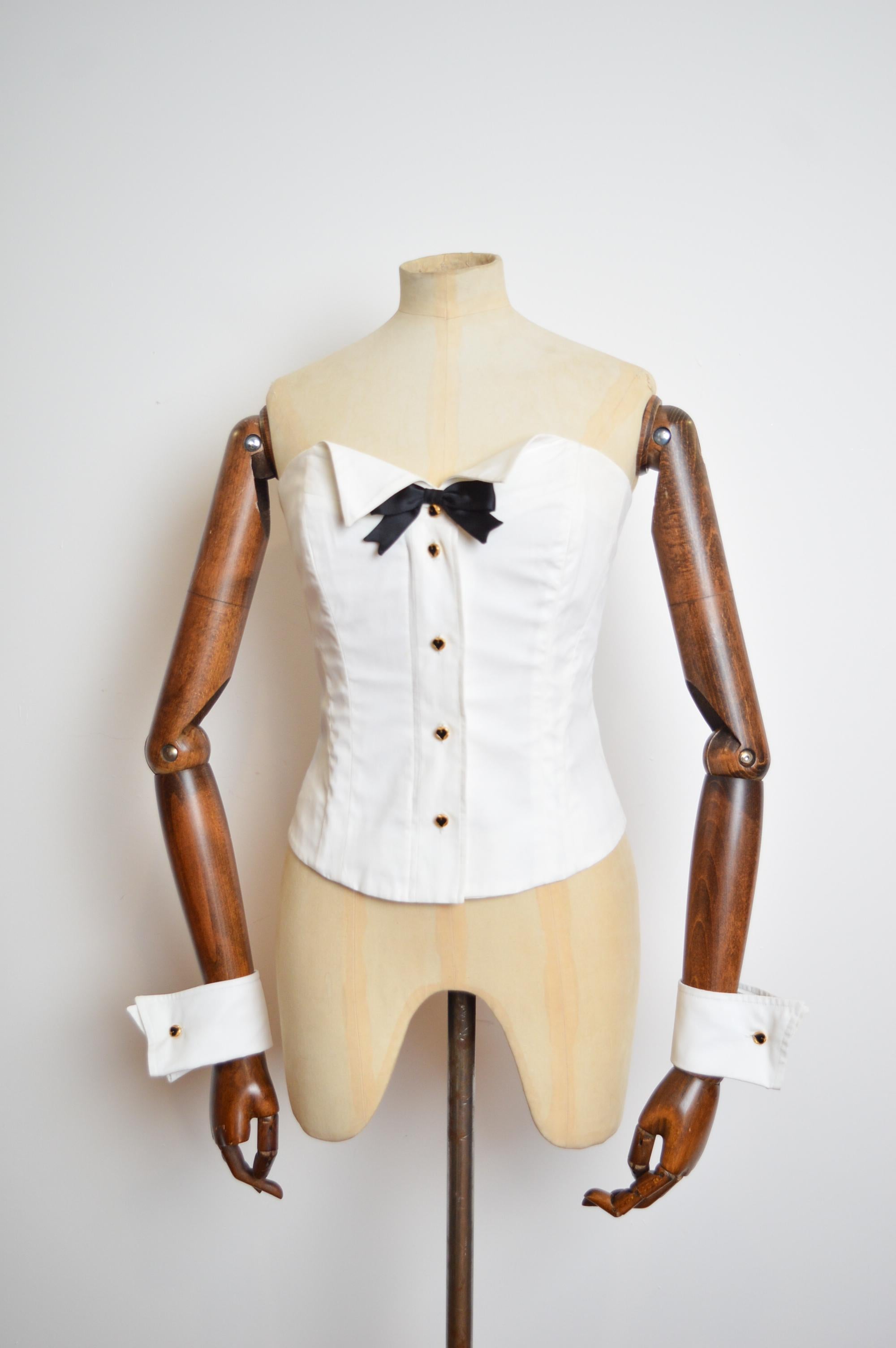 1990's Moschino Couture Play boy Bunny style Novelty Tuxedo Corset and matching Cuffs set !
MADE IN ITALY
100% Cotton 
Zip down front with decorative button closure 
Matching Wrist Cuffs  
Pit to Pit; 17”
Top to Hem; 14”
Waist; 28”
Size; Recommended