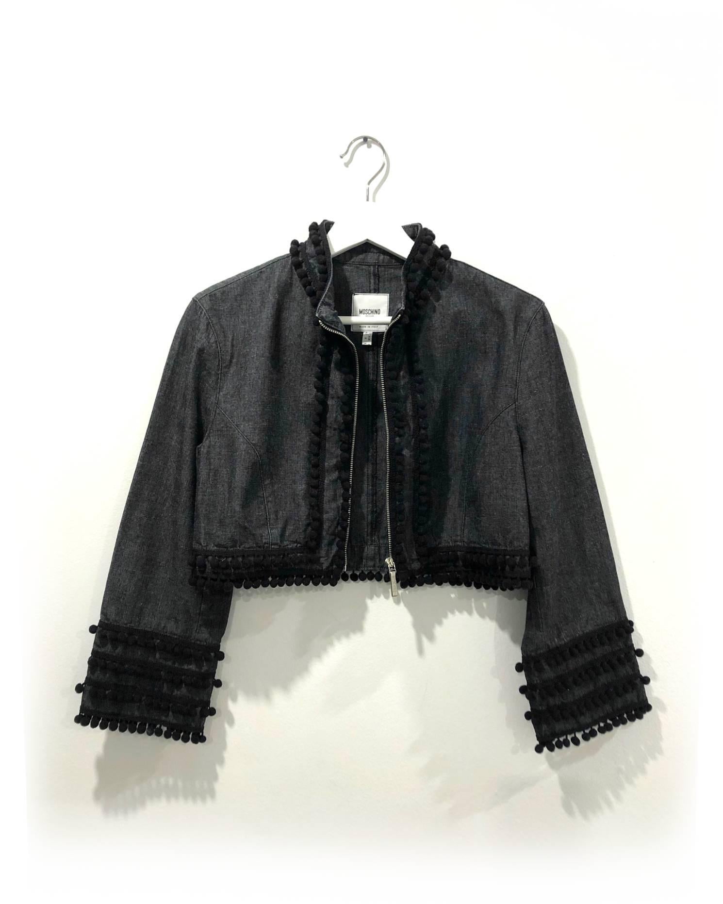 Moschino-Bolero aus Denim von 1990, dunkelblau/grau, neutrale Denimfarbe, mit schwarzem Bommelbesatz im Stil von Spanish Matador an den Rändern und mehreren Reihen an den Ärmeln. Gekürzter Body mit Reißverschluss und Branding am Reißverschluss. Die