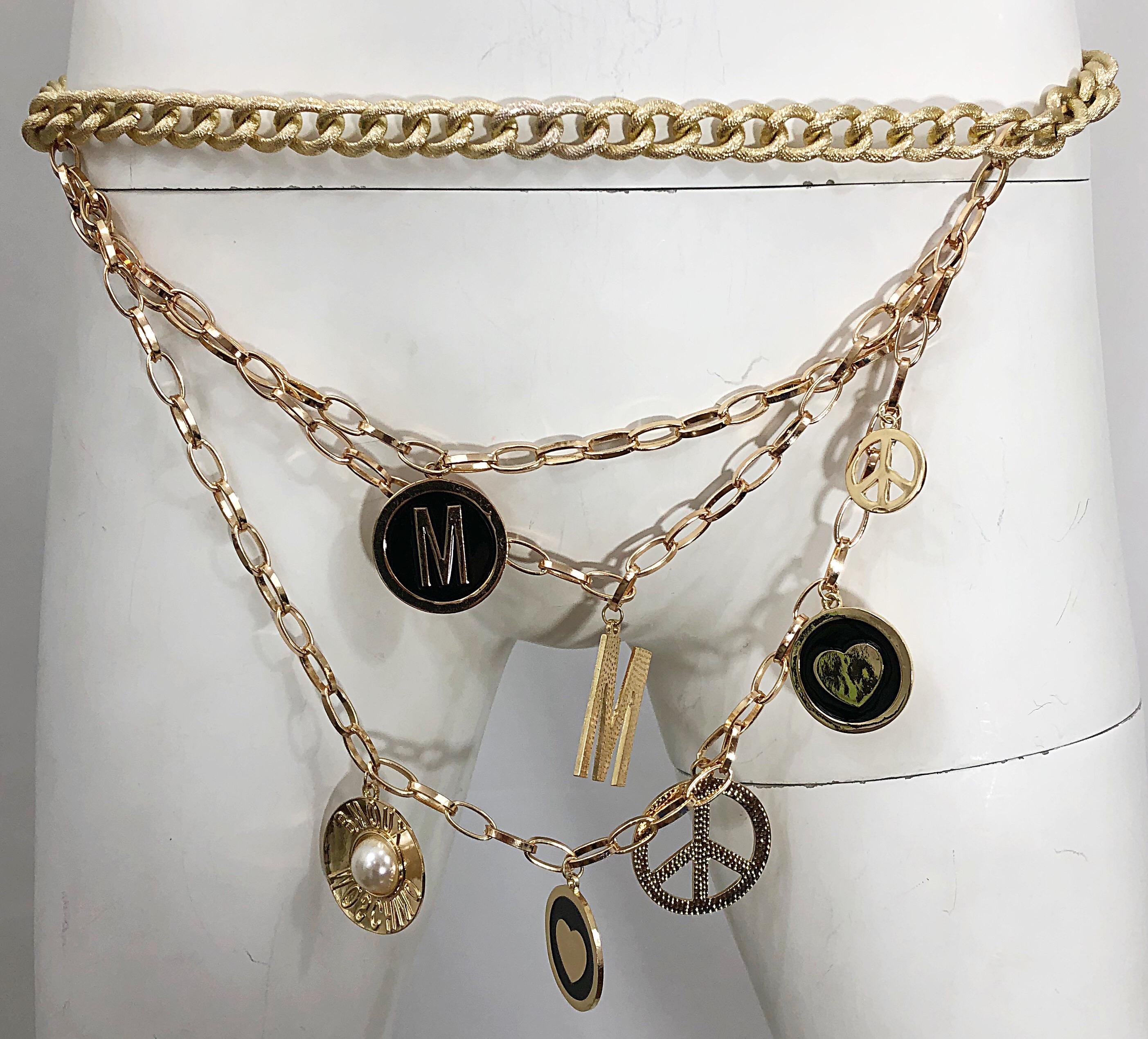 Iconic and chic vintage 90s MOSCHINO gold charm belt or necklace! Features a muted gold chain with gold tiers of chain. Large 'M' charm, with charms of hearts, peace signs. An additional charm has a pearl and Moschino spelt backwards. This rare gem